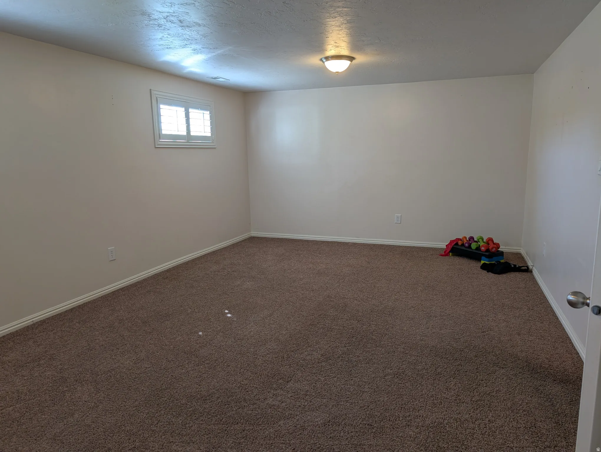 Spacious multipurose room featuring neutral carpeting, light-toned walls, and a single window with plantation-style shutters