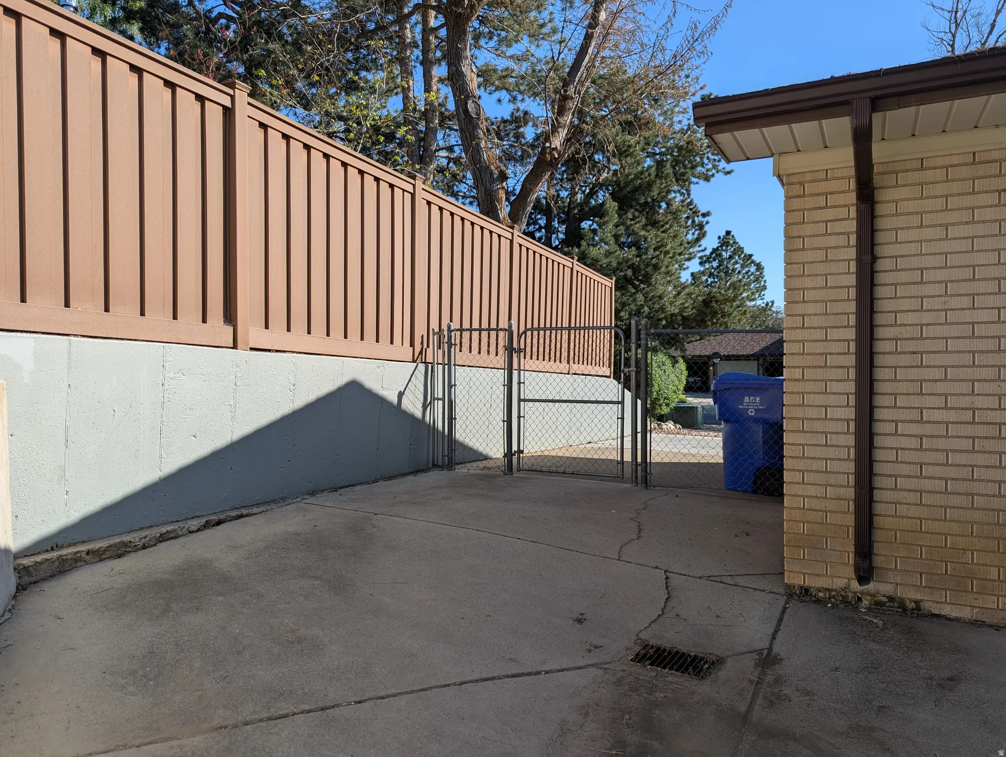 Paved concrete surface bordered by a light brown privacy fence atop a concrete retaining wall