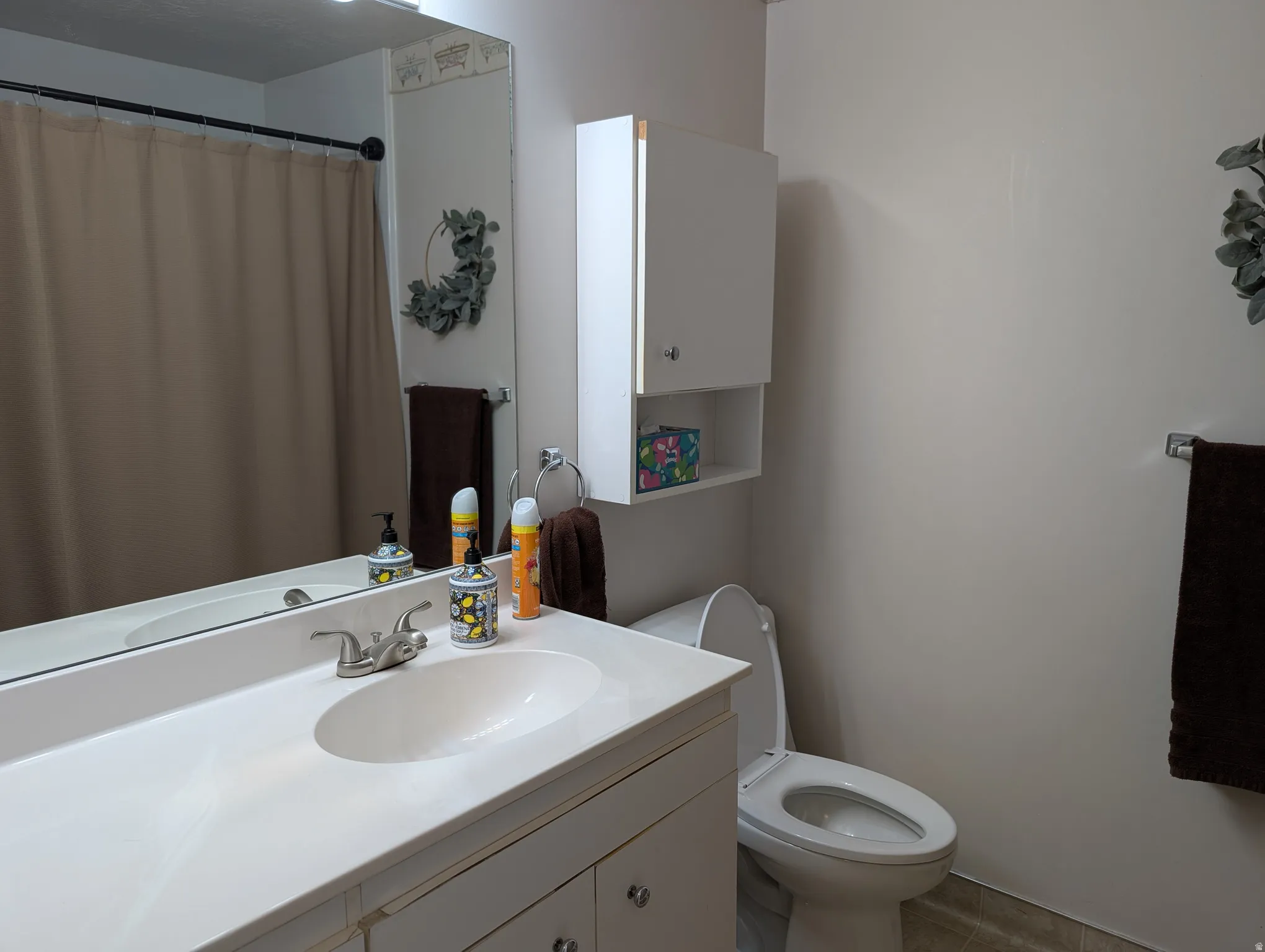 Bathroom vanity with integrated sink and chrome faucet, large wall mirror, and overhead cabinet storage