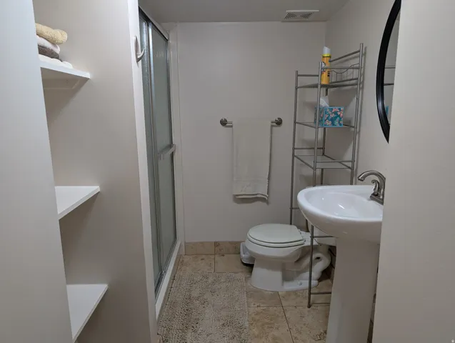 Bathroom featuring a pedestal sink with a brushed nickel faucet, a toilet, and a shower with a sliding glass door