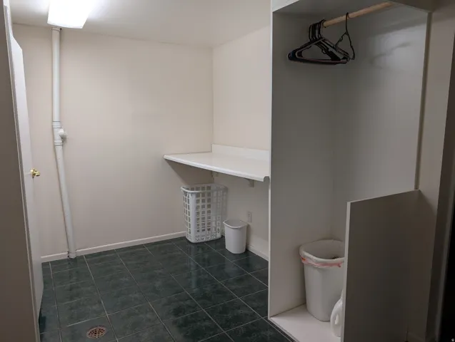 Laundry area featuring dark green square floor tiles, a built-in white countertop, and a clothes hanging rod within an alcove
