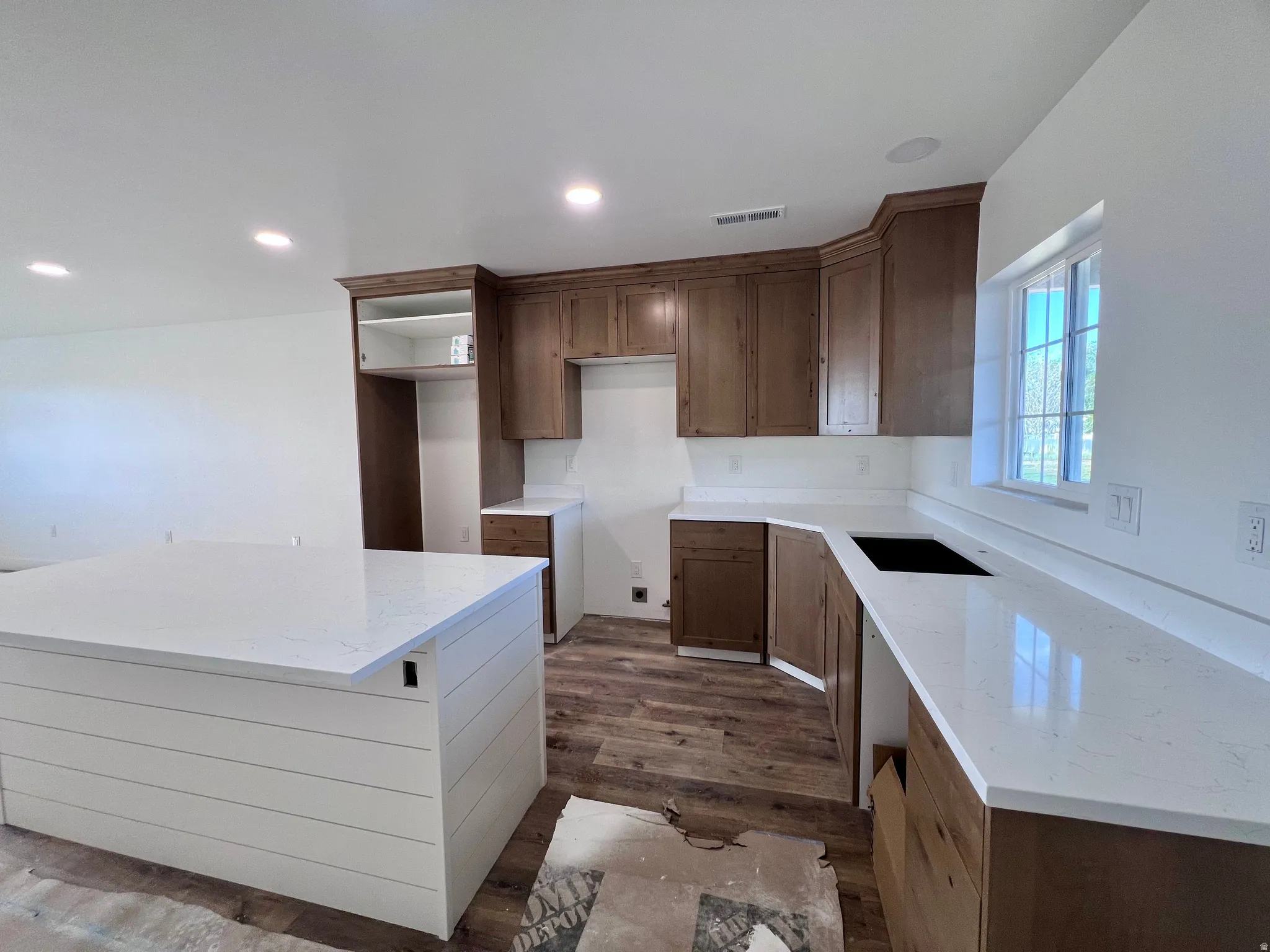 Kitchen featuring a white shiplap island with a solid surface countertop, wood-finish flooring, recessed lighting, wood cabinetry, and a window above the countertop