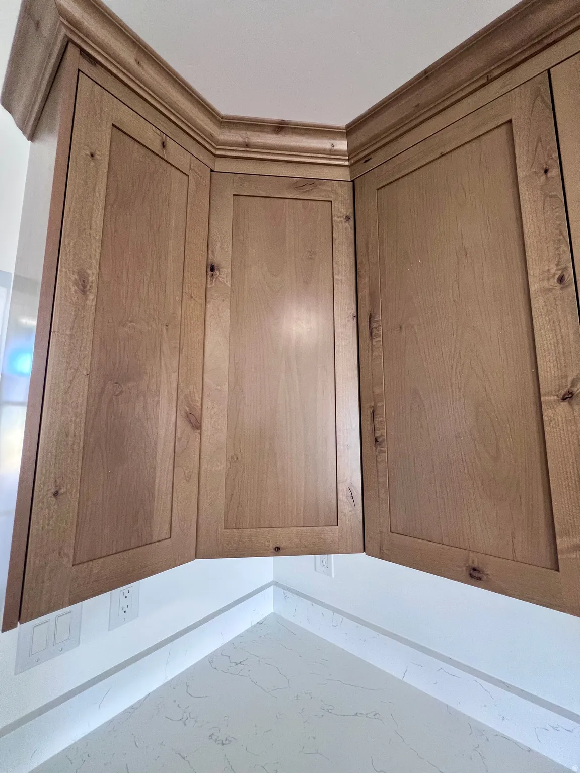 Corner cabinetry with natural wood-finish shaker-style doors and crown molding