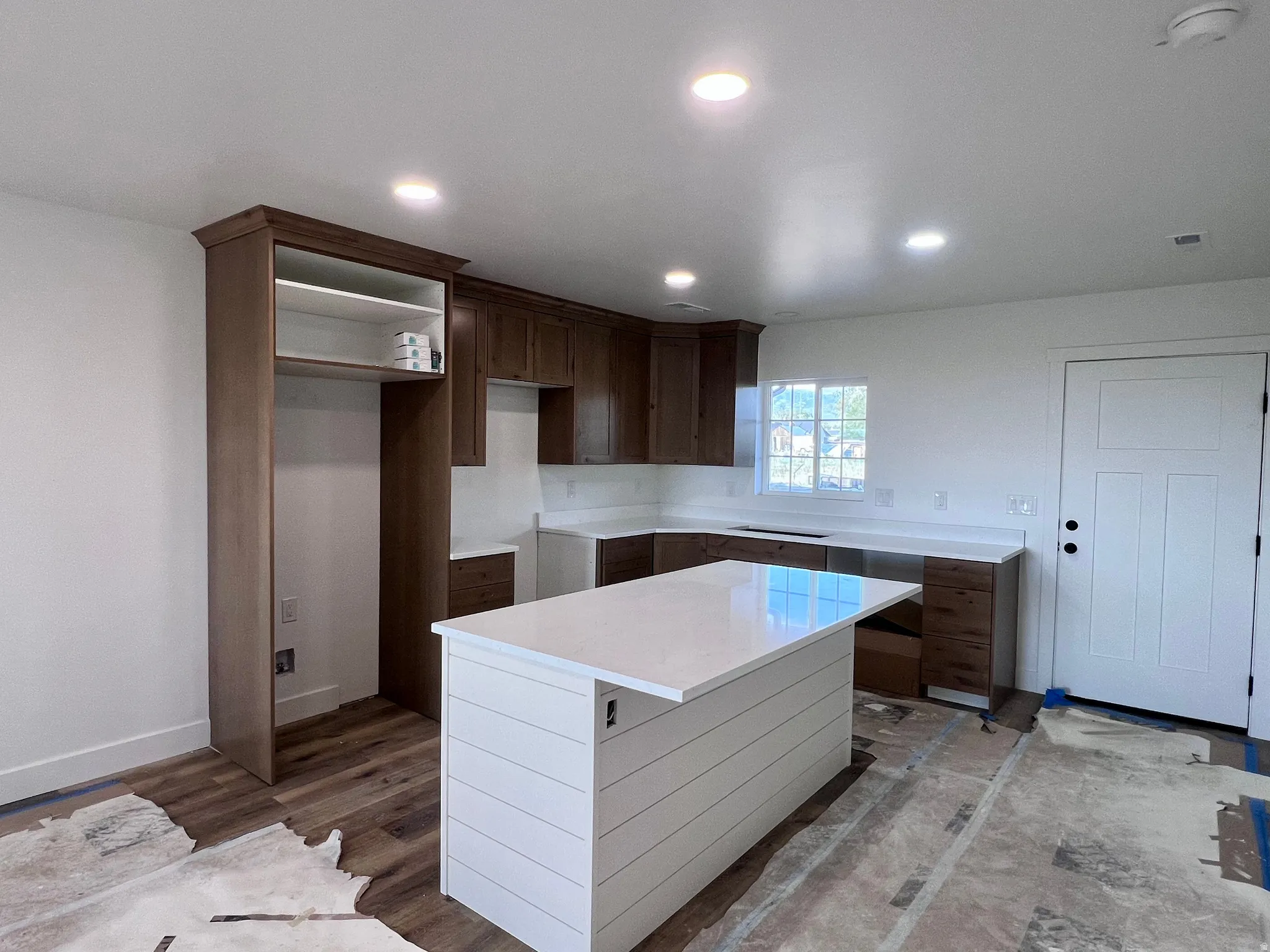 Kitchen featuring a central island with shiplap base, wood-finish cabinetry, light-toned countertops, recessed lighting, and a window