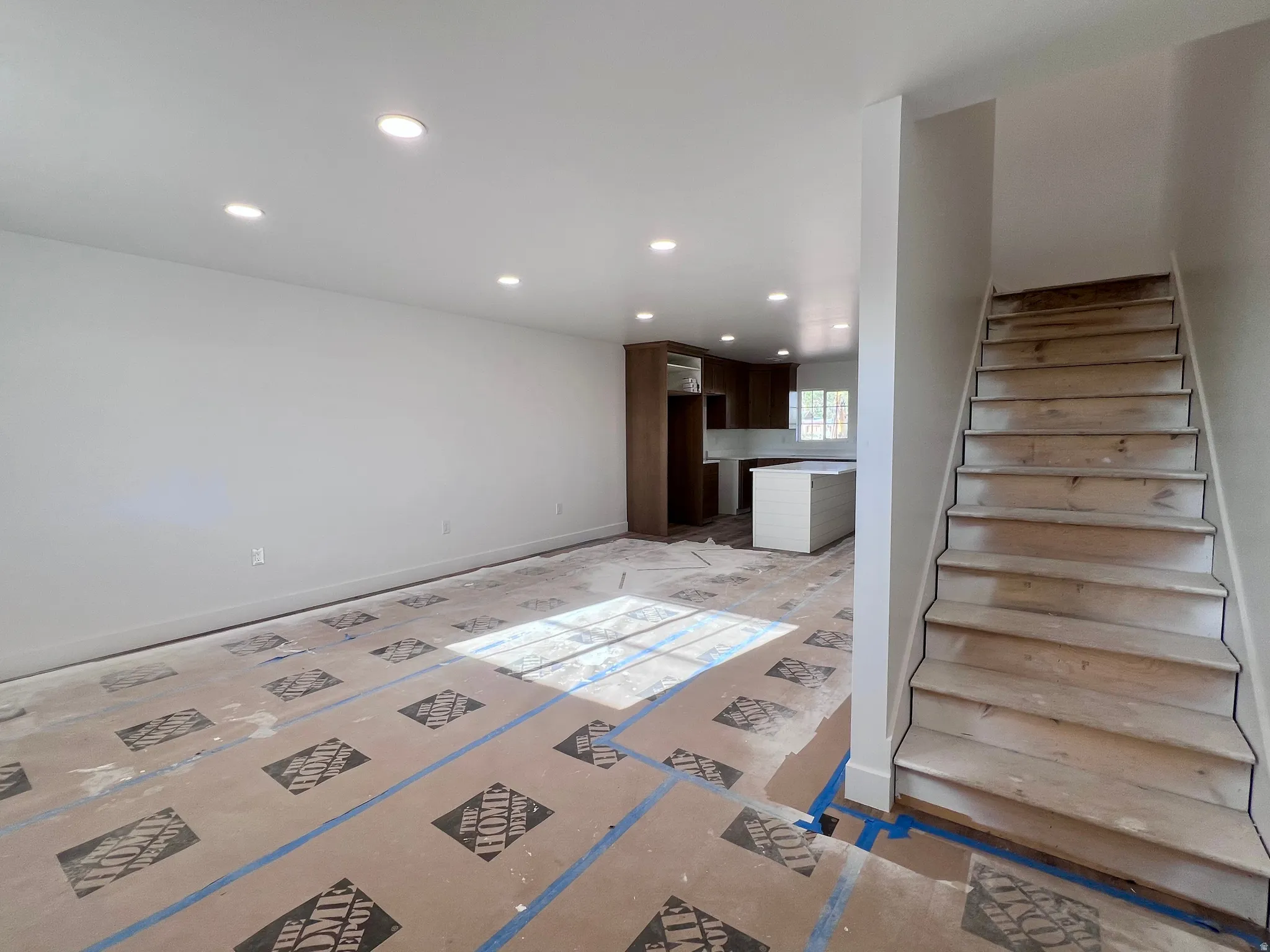 Open-concept living area with recessed lighting, raw wood staircase, and a kitchen featuring dark wood cabinetry, light-toned countertops, and a center island