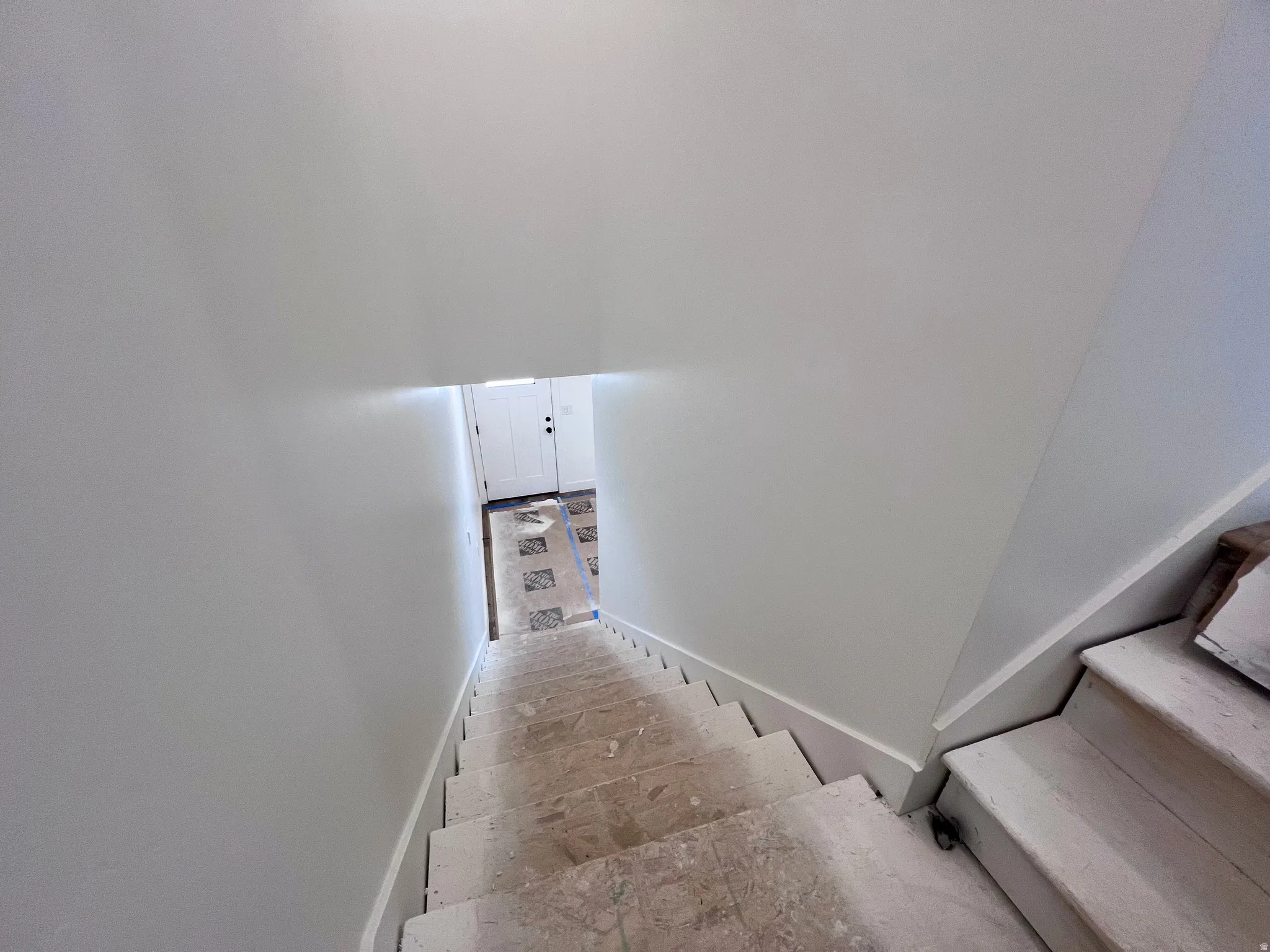 Stairwell with light-colored risers and treads leading to a lower level with patterned flooring and a panel door