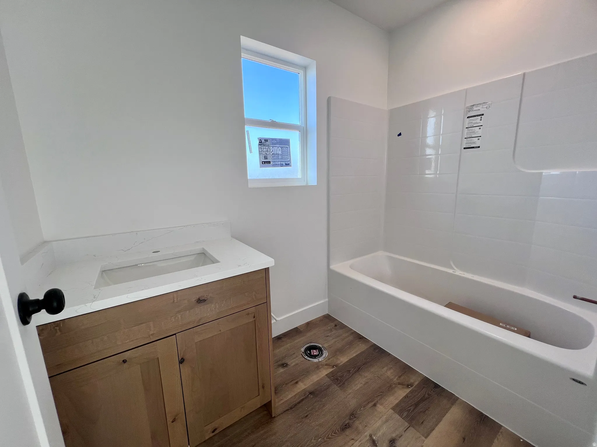 Bathroom featuring a wood-finish vanity with an integrated sink, a white countertop, wood-finish flooring, a white bathtub, and white subway tile surround