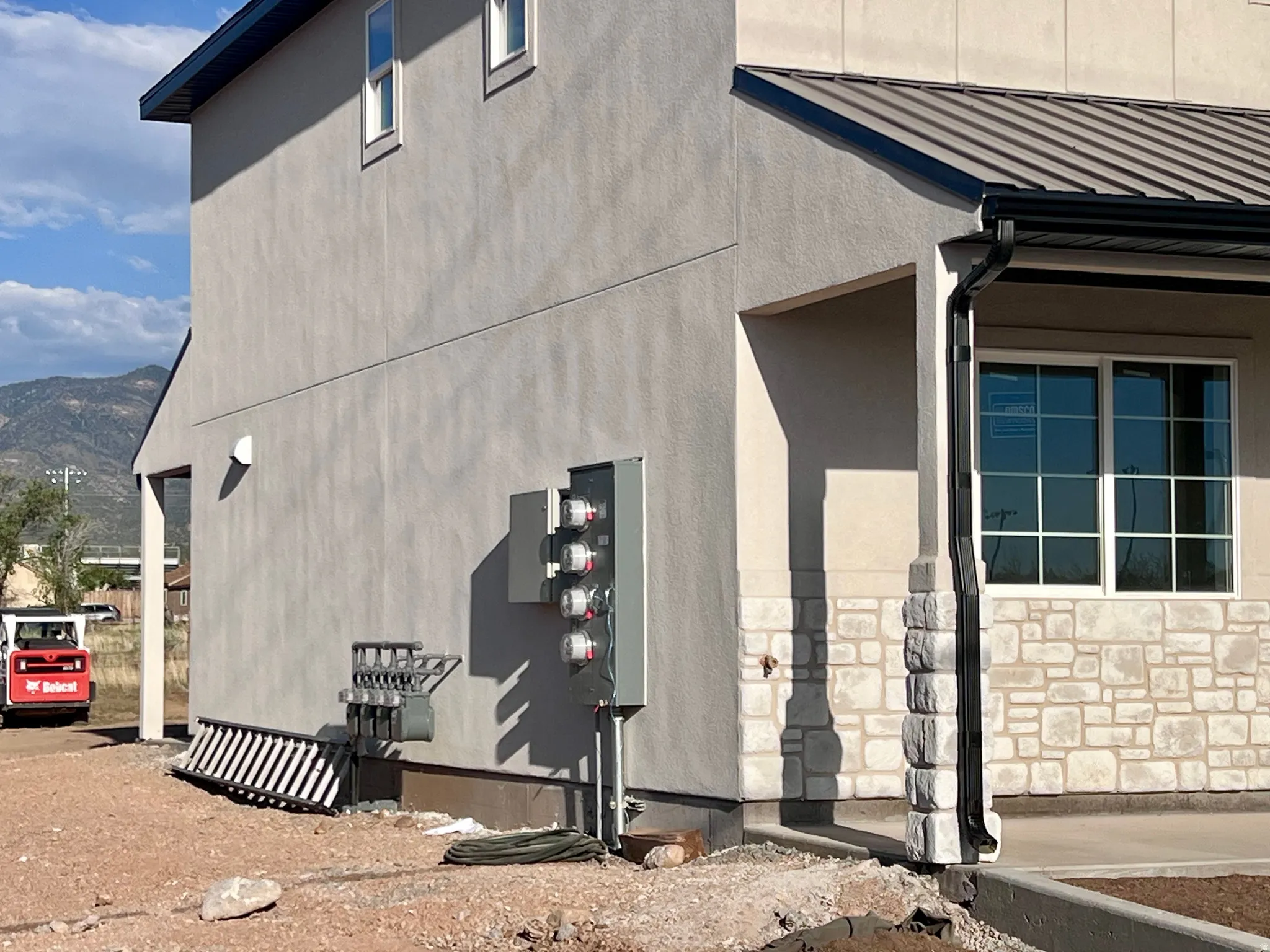 Stucco exterior with stone accent detailing, metal roofing, and multiple utility meters