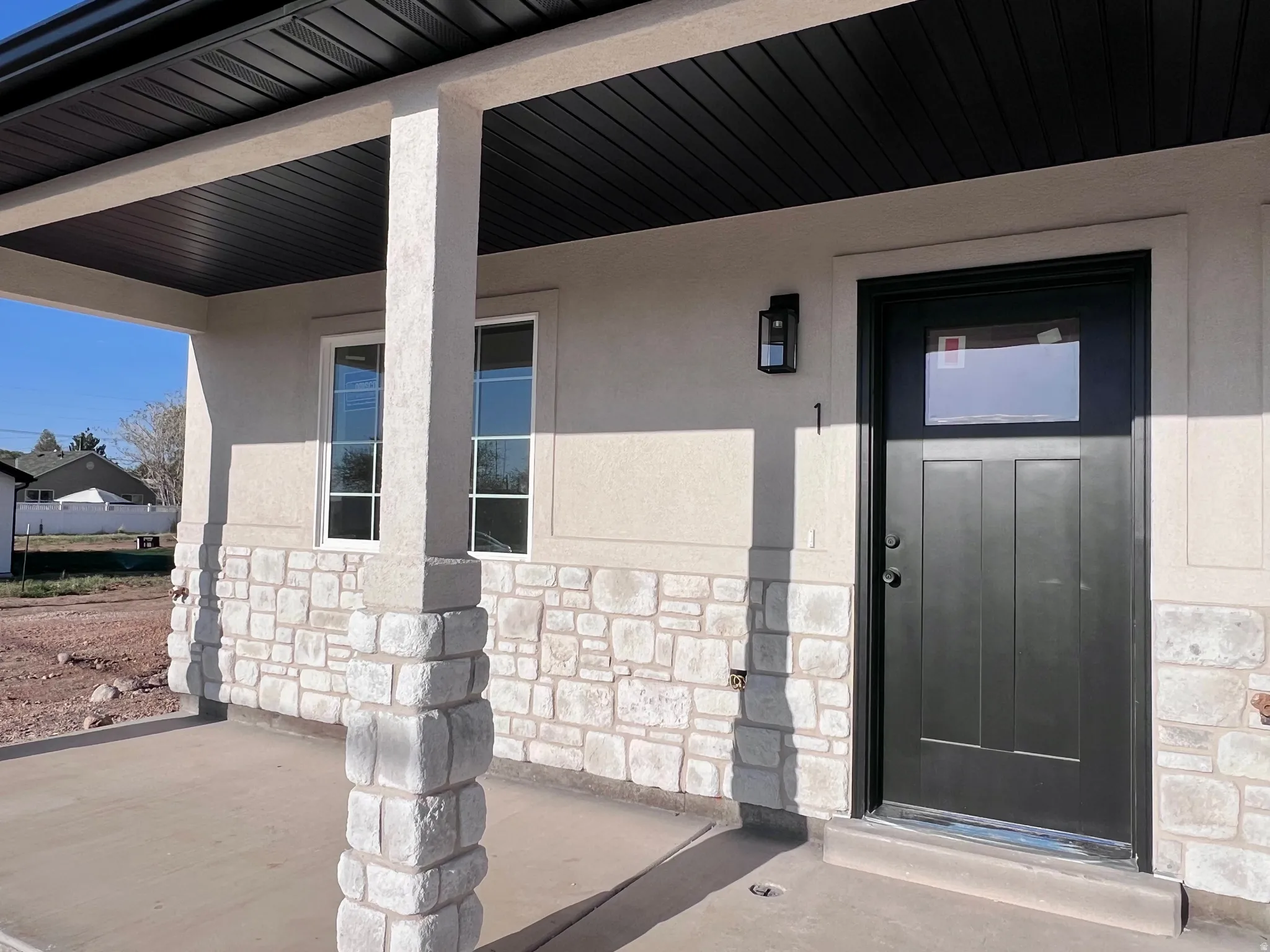 Inviting entry featuring a covered porch, stone veneer accents, and a black paneled door with an integrated window