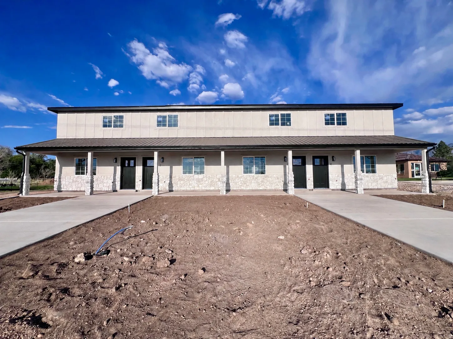 Two-story multi-unit dwelling with a covered porch featuring stone columns and a metal roof