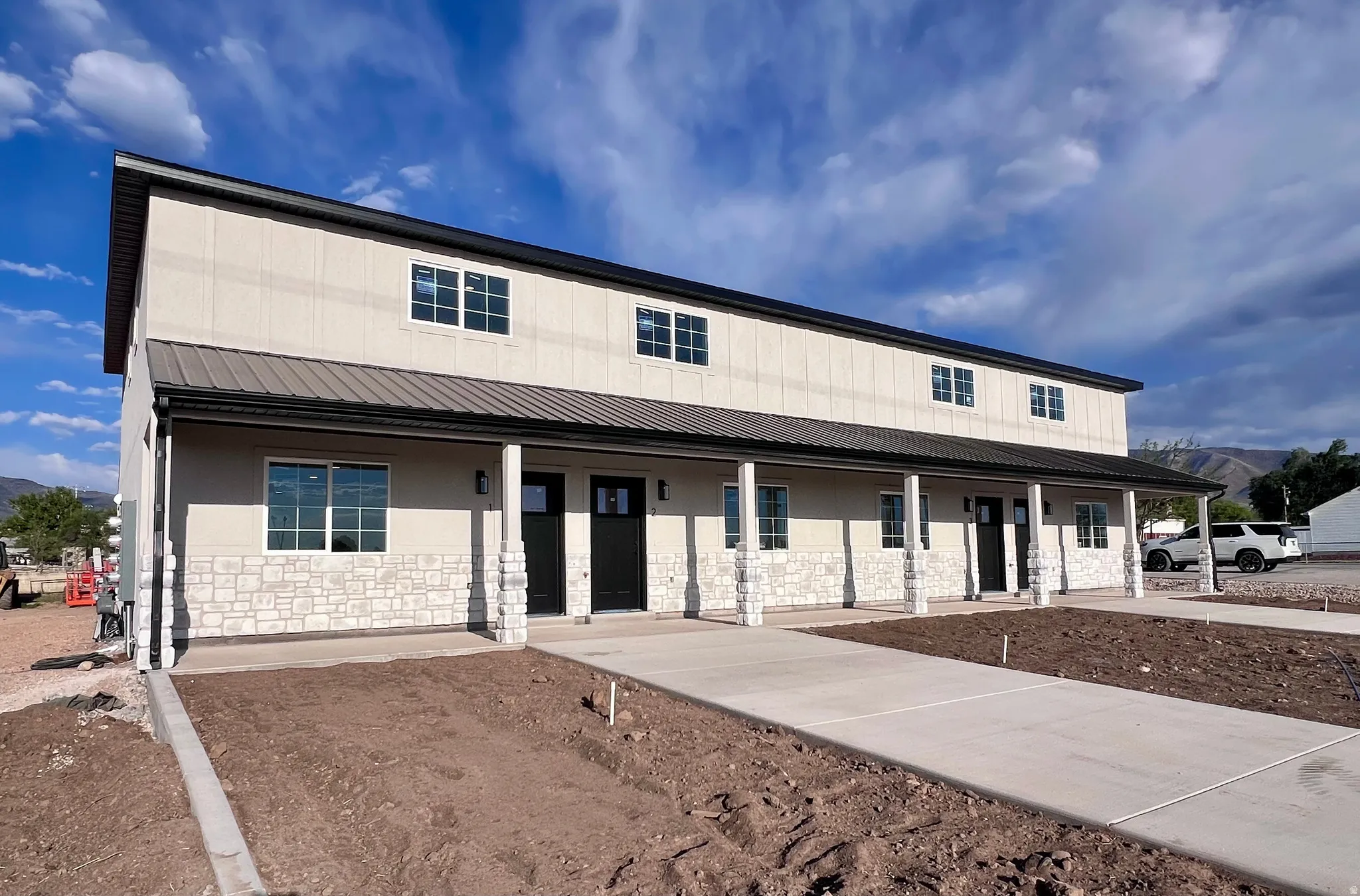 Modern multi-unit building featuring stone accents, a covered porch with stone-wrapped columns, a metal roof, and individual entry doors