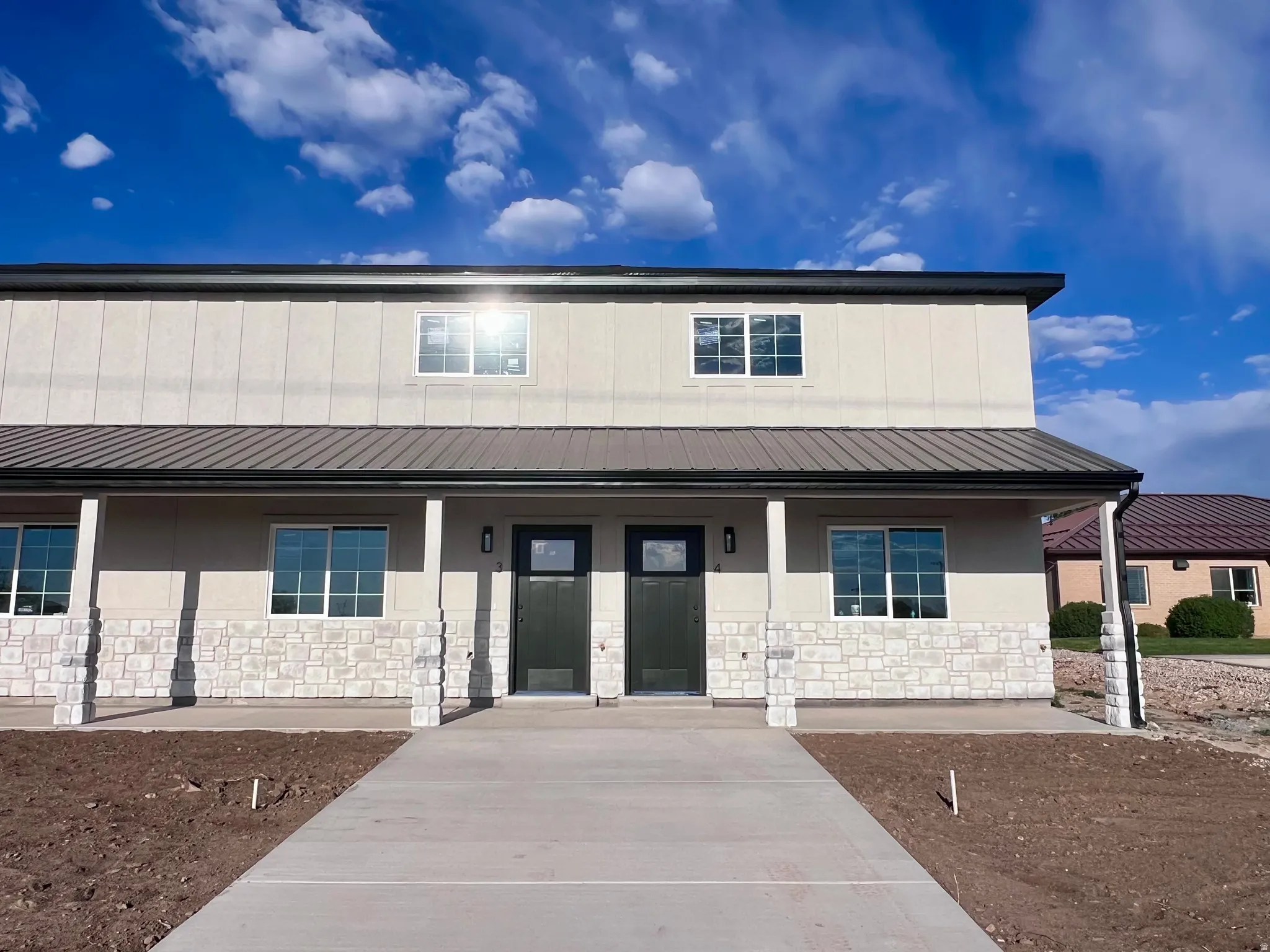 Modern duplex exterior featuring a metal roof, stone facade, and concrete walkway