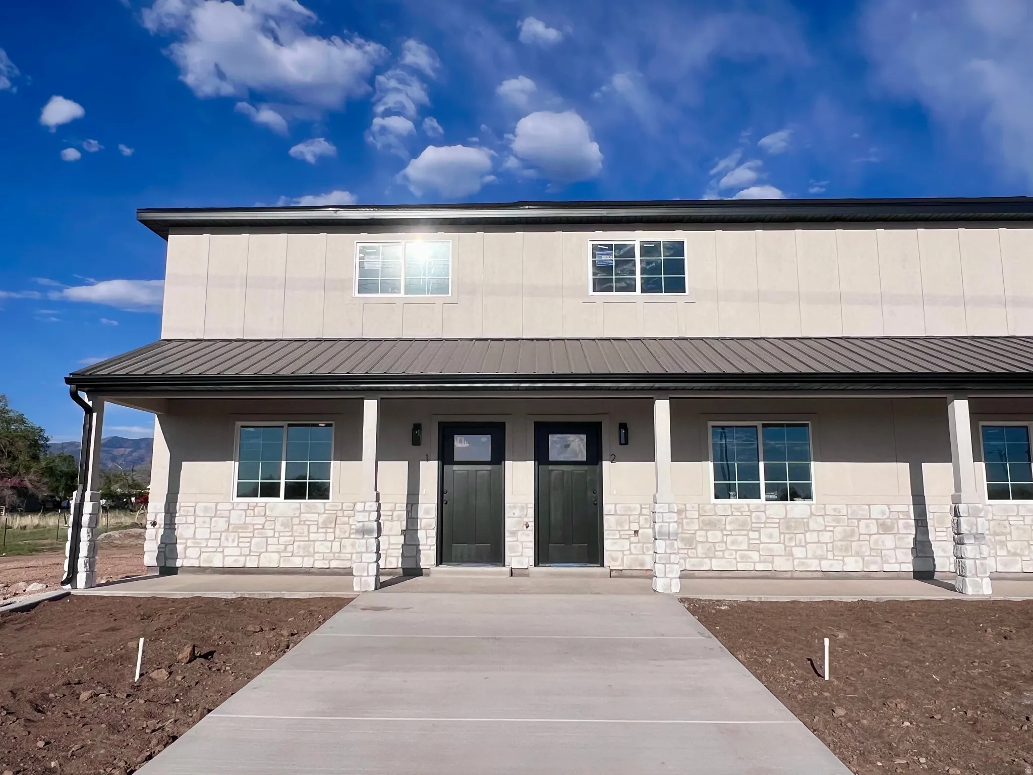 Modern stucco exterior with stone accents and a covered front porch featuring a dark metal roof