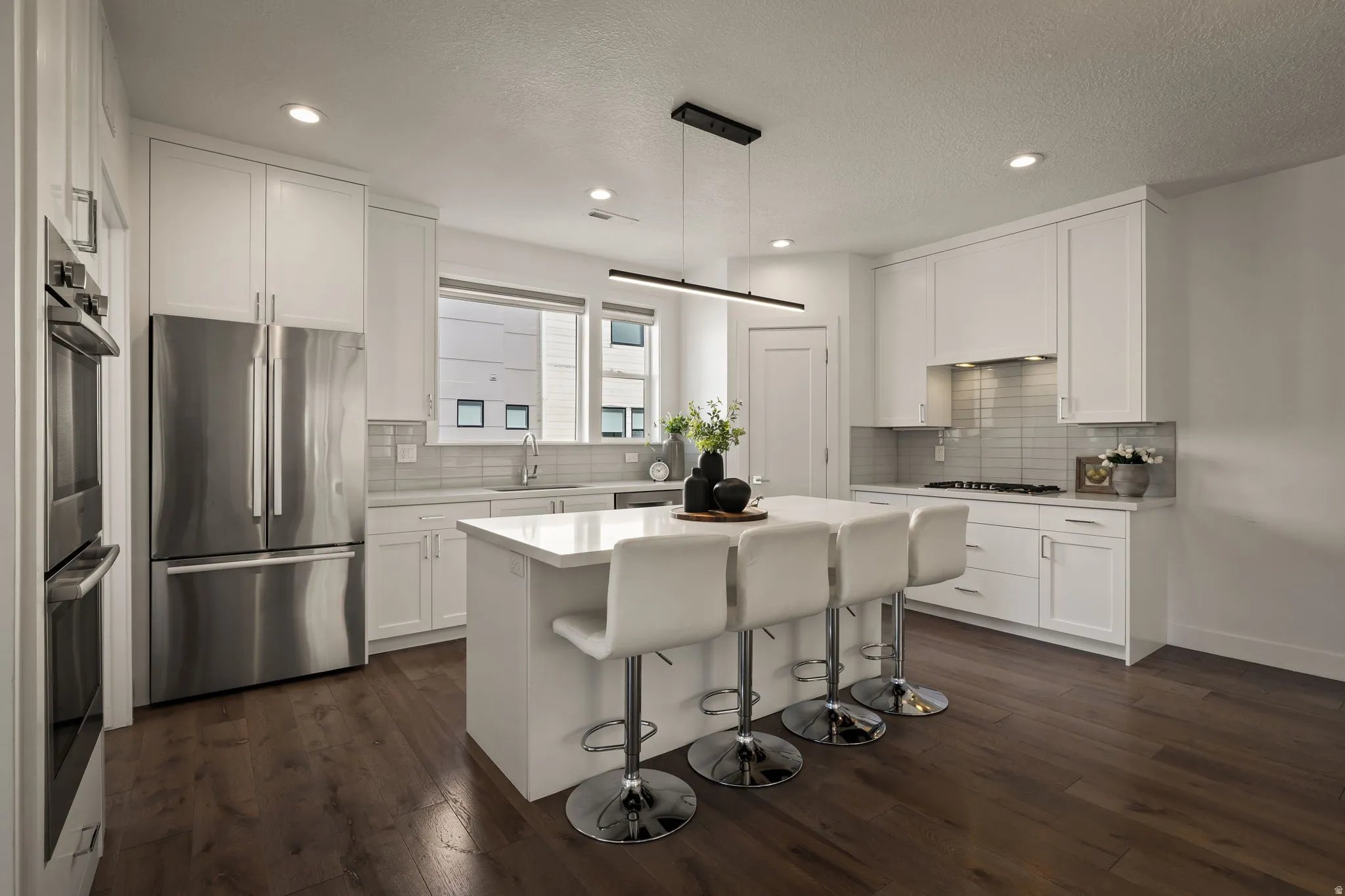 Kitchen with stainless steel appliances, a breakfast bar, white cabinetry, dark wood-style floors, and a textured ceiling