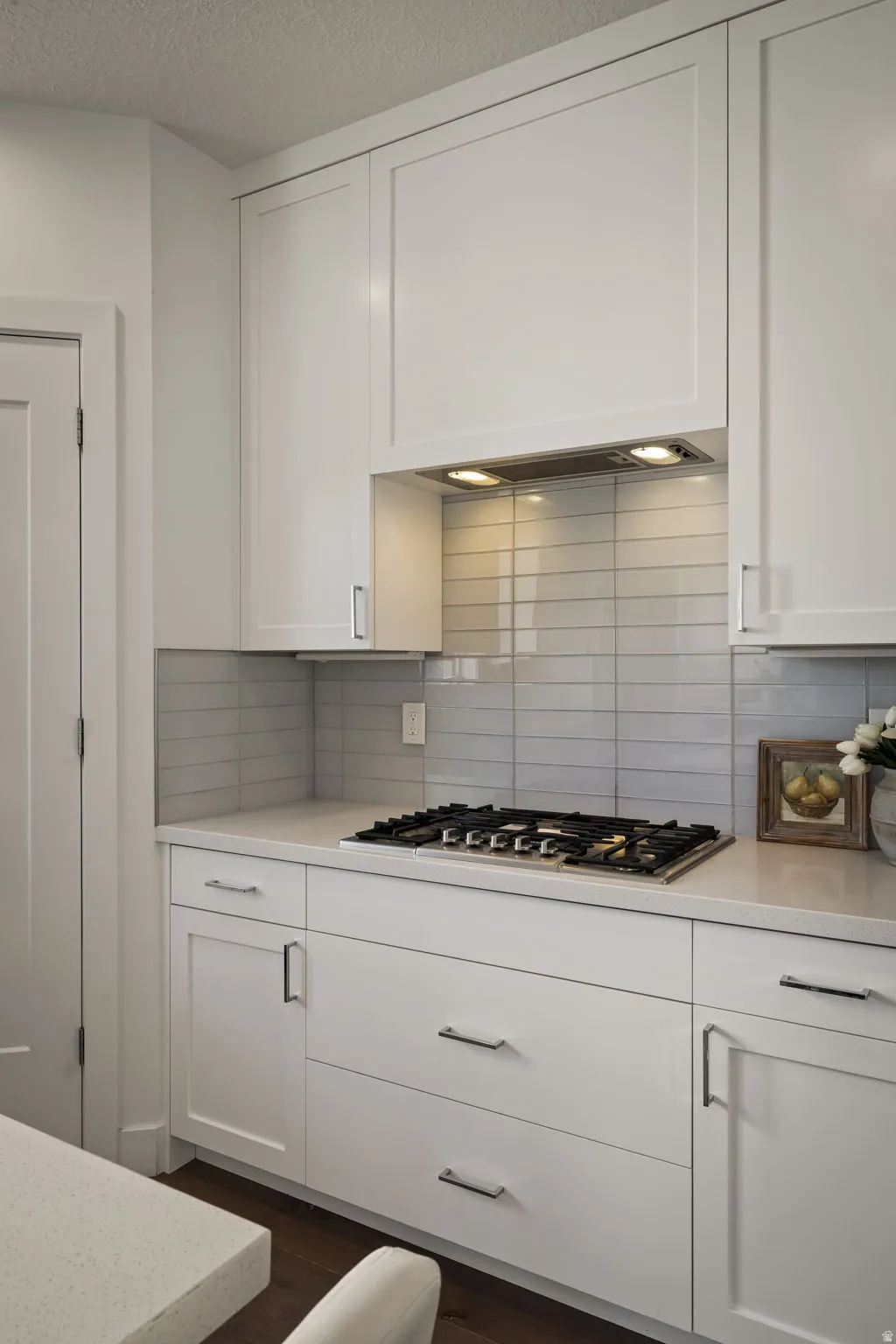 Kitchen featuring white cabinets, dark wood-style flooring, stainless steel gas stovetop, a textured ceiling, and light stone counters
