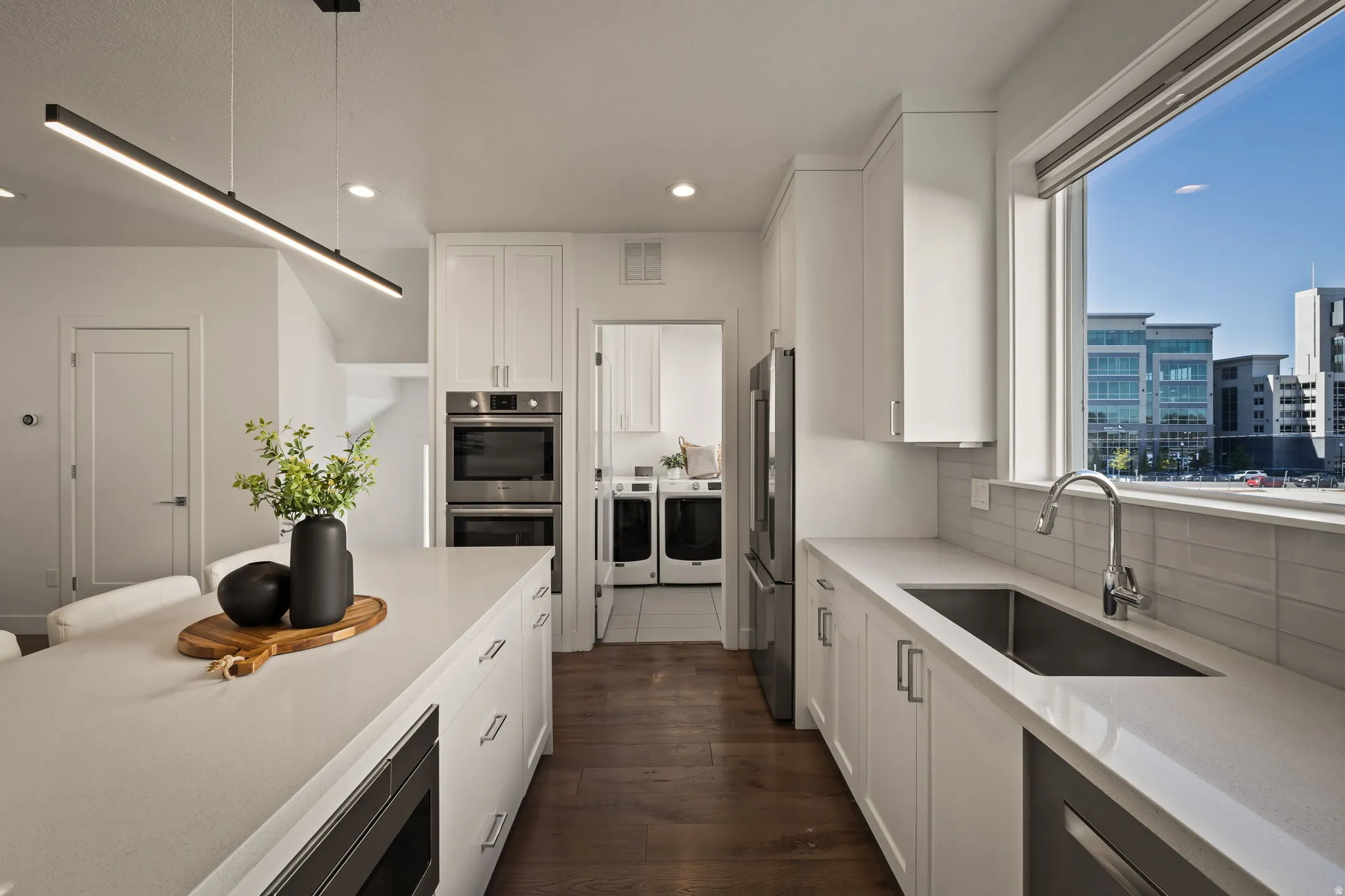 Kitchen with washer and clothes dryer, white cabinetry, stainless steel appliances, dark wood-style floors, and light stone countertops