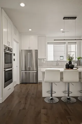 Kitchen featuring stainless steel appliances, white cabinetry, a kitchen breakfast bar, dark wood finished floors, and recessed lighting