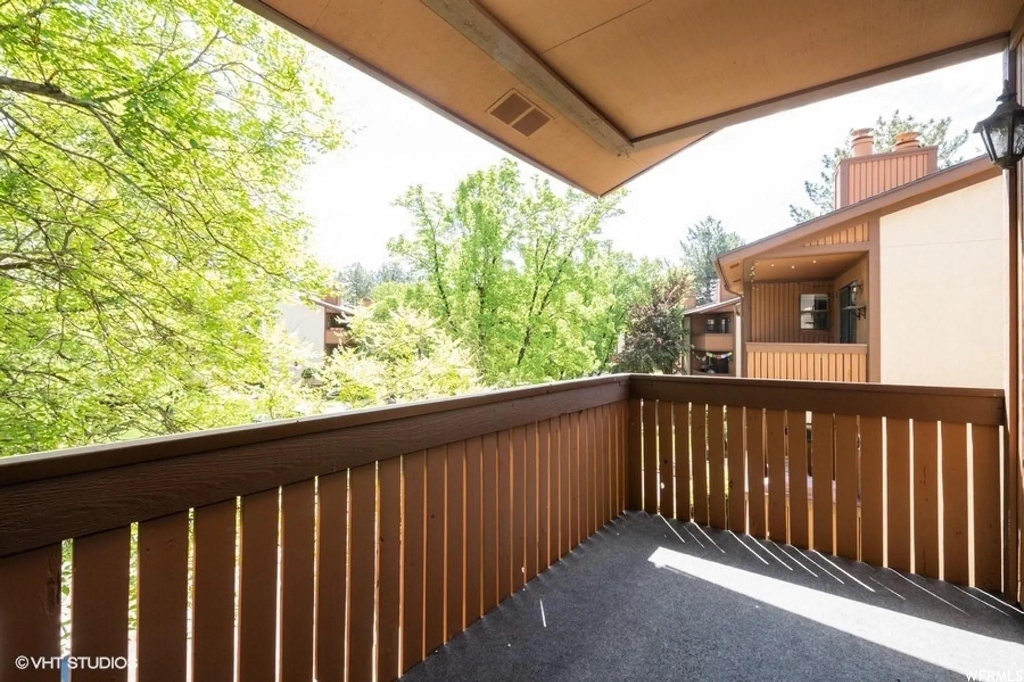 Private balcony featuring a wood-slat railing, carpet flooring, and an exterior wall lantern