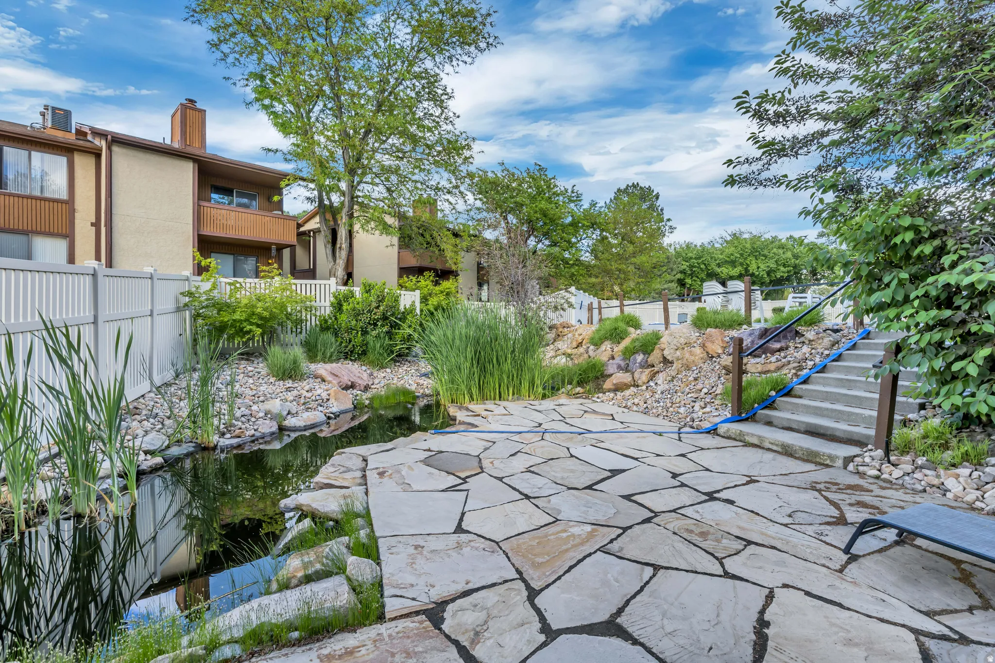 Spacious outdoor area featuring a flagstone patio, natural water feature, concrete steps, and established landscaping
