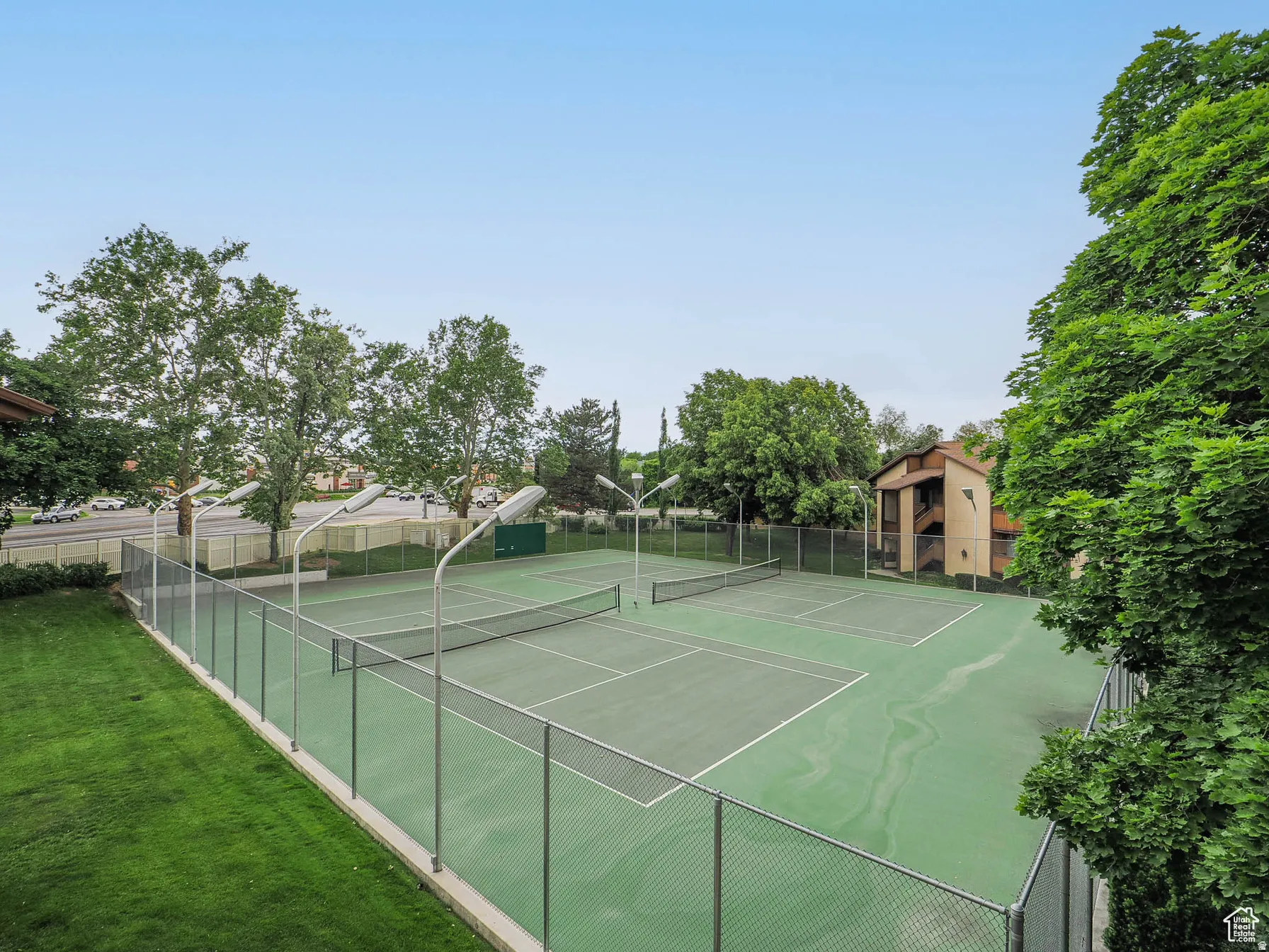 Two tennis courts with a hard-court surface, surrounded by chain-link fencing and mature trees