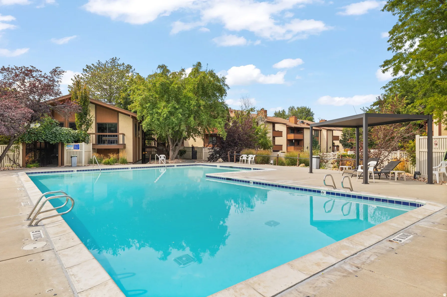 Outdoor swimming pool with concrete decking, surrounded by mature trees and residential structures