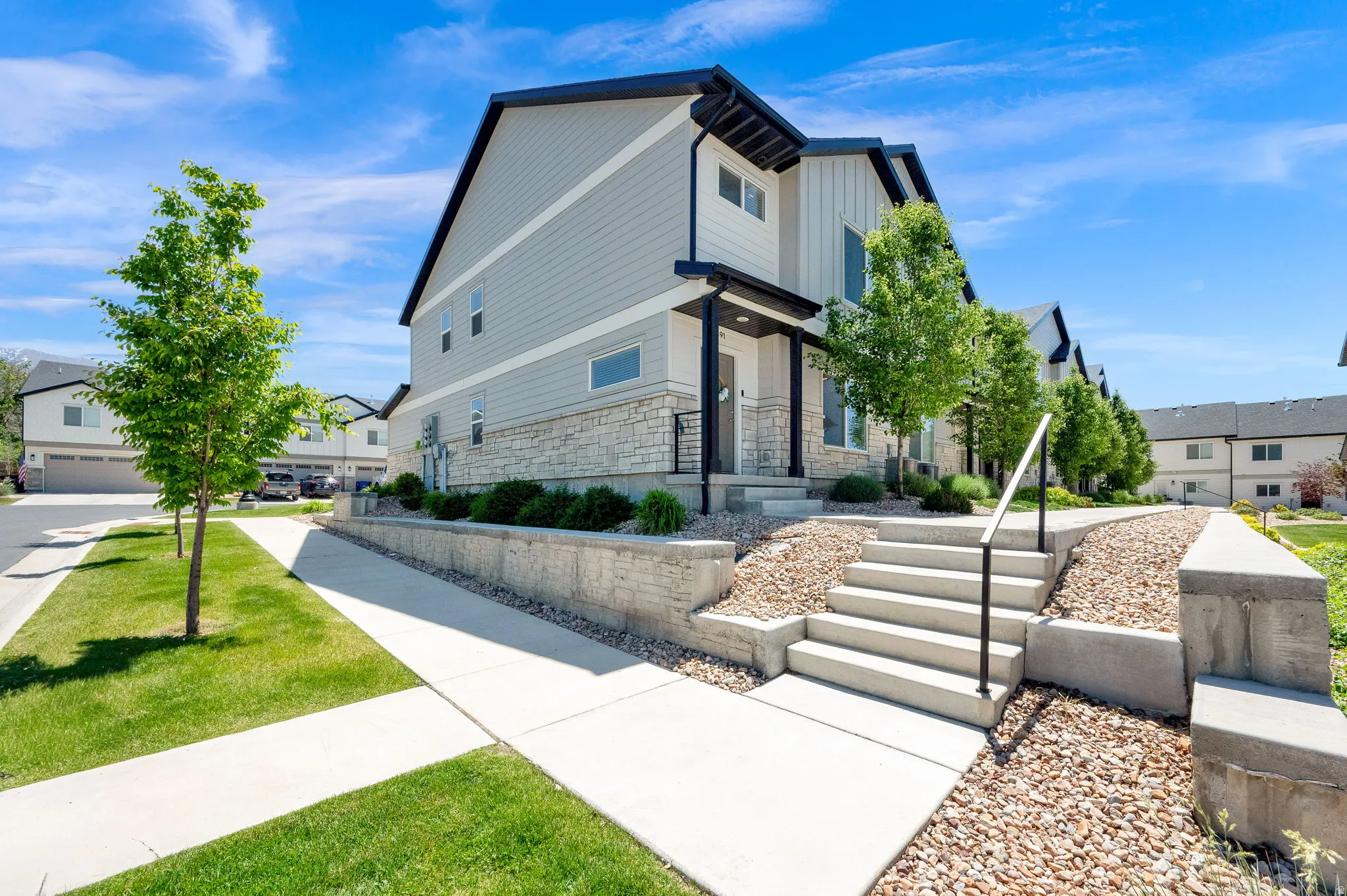 Contemporary exterior featuring light gray siding, stone veneer accents, and a dark trim roofline