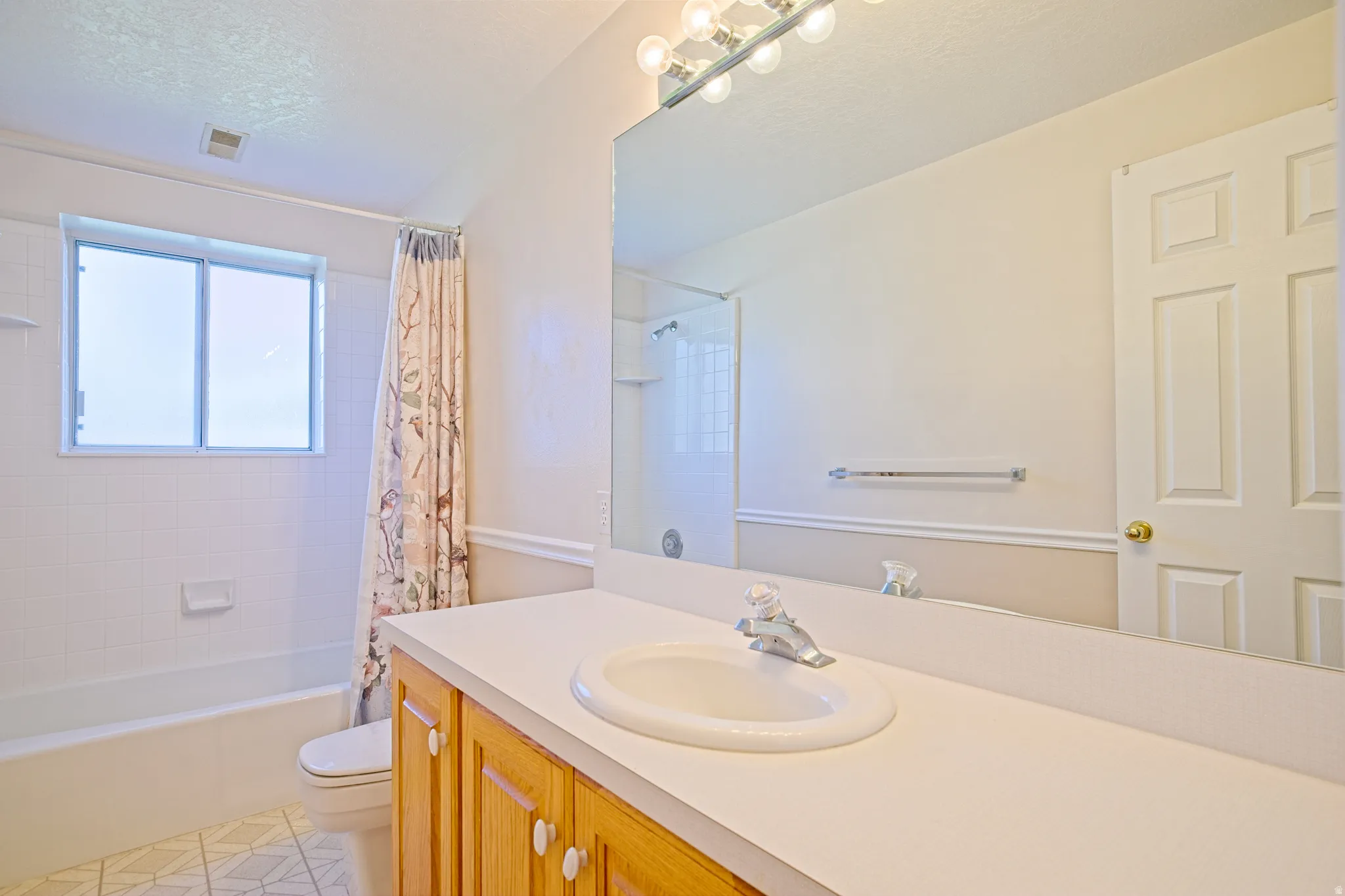 Bathroom vanity with a white countertop and integrated sink, accompanied by a large wall-mounted mirror and a light fixture with multiple bulbs