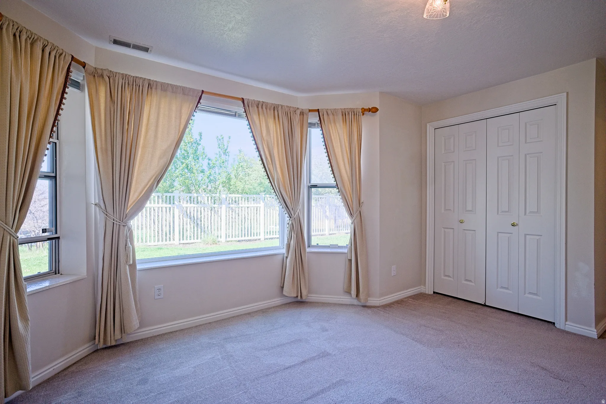 Bay window with expansive glass, carpet flooring, white bi-fold closet doors, white baseboards, and a ceiling-mounted light fixture
