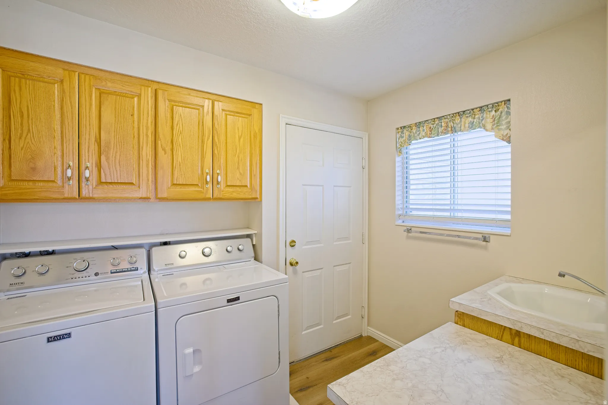 Functional utility space featuring wood-finish flooring, a built-in utility sink with countertop, and overhead wood cabinetry. Laundry room with garage door entrance.