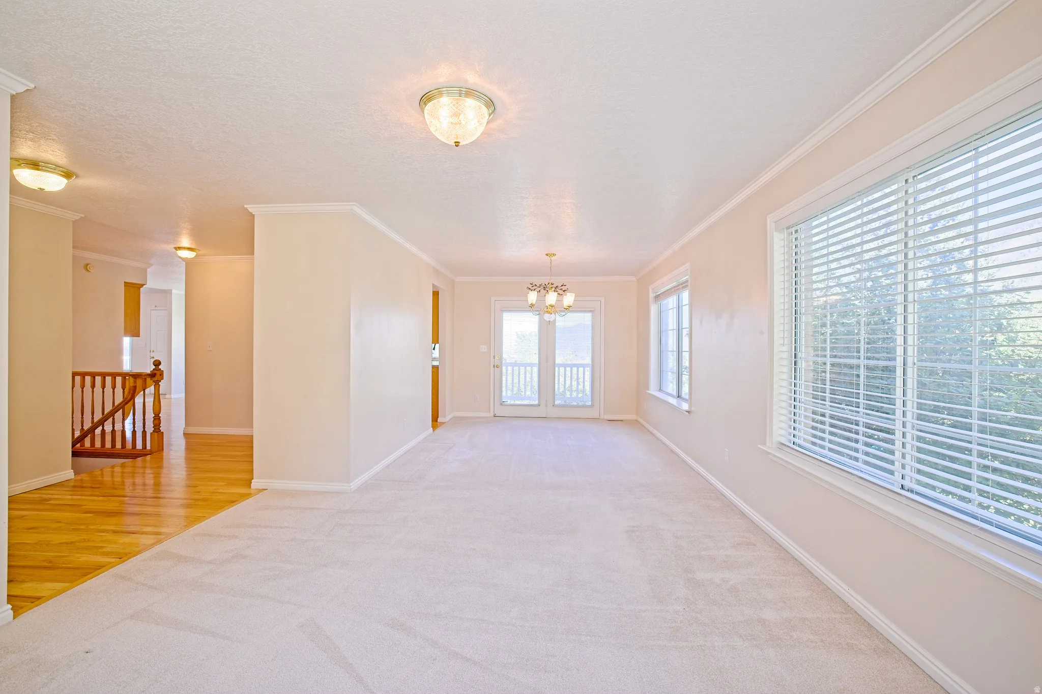 Spacious carpeted living area featuring white trim, a chandelier, and French doors