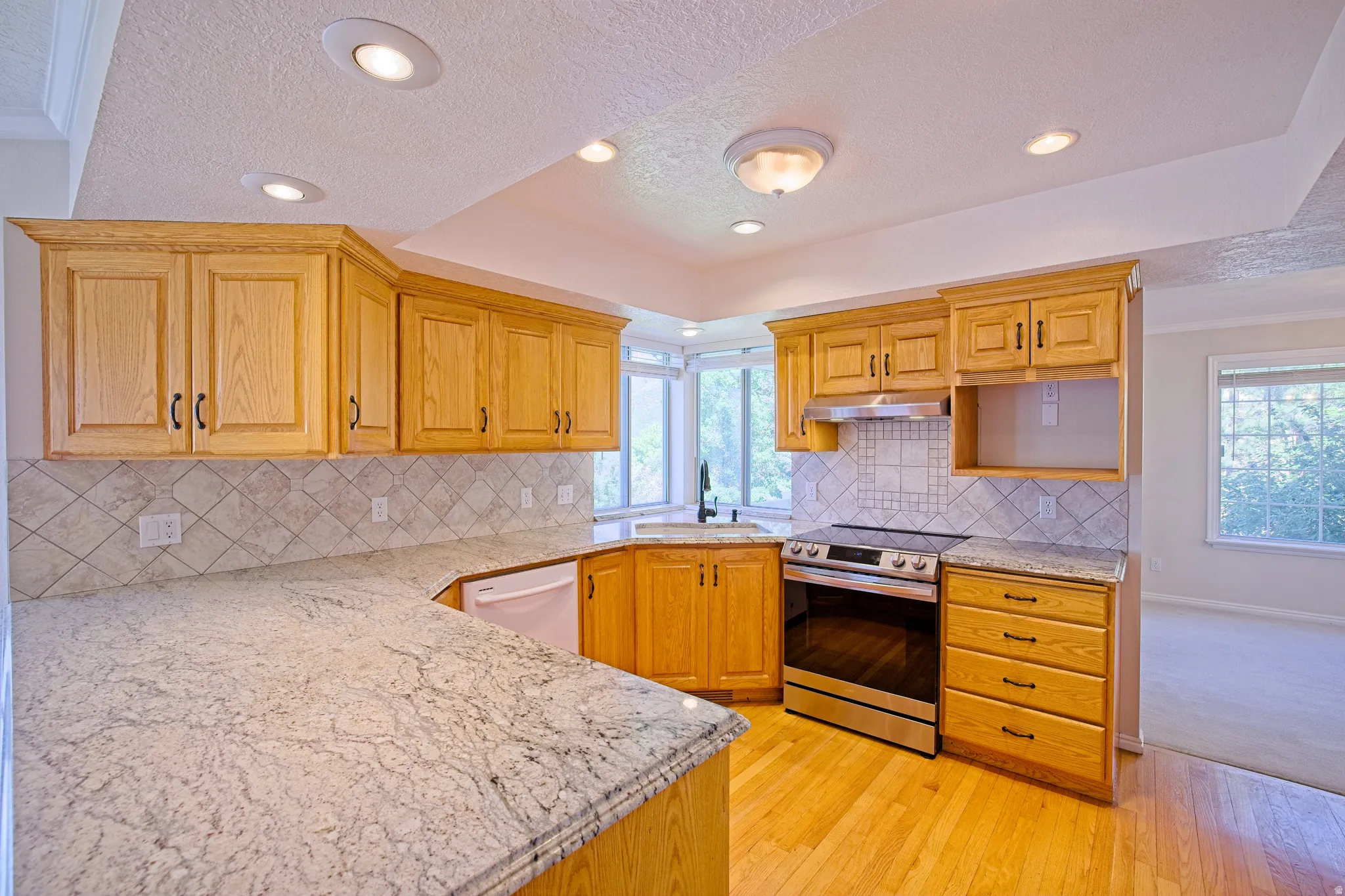 Kitchen featuring wood-finish cabinetry, light-toned countertops, a tile backsplash, stainless steel range, and wood-finish flooring