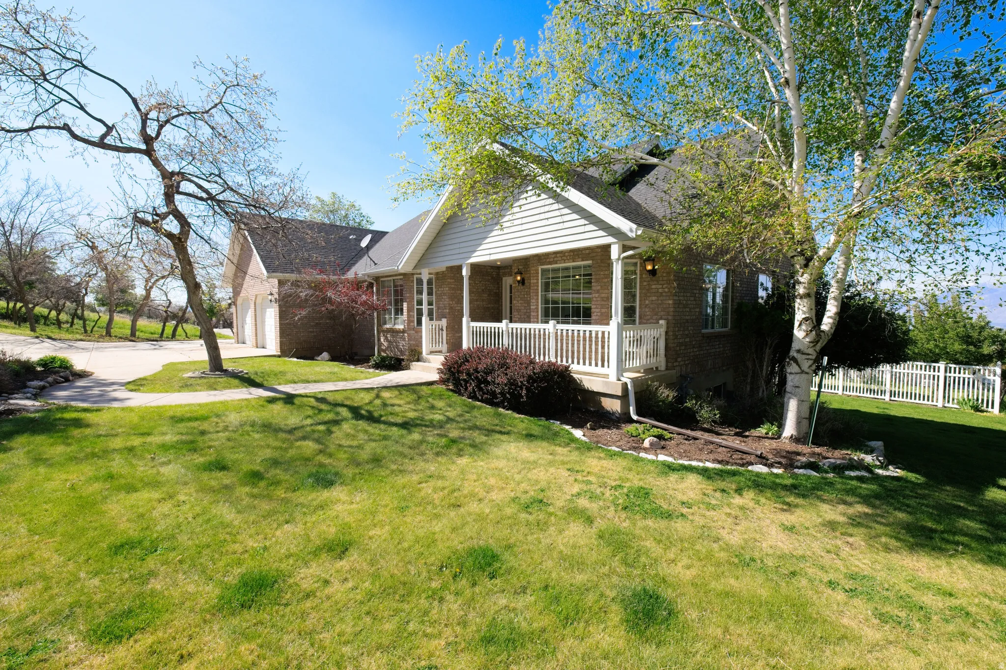 Traditional brick and siding residence featuring a covered front porch with white railing, a two-car garage, and a white picket fence enclosing a portion of the property