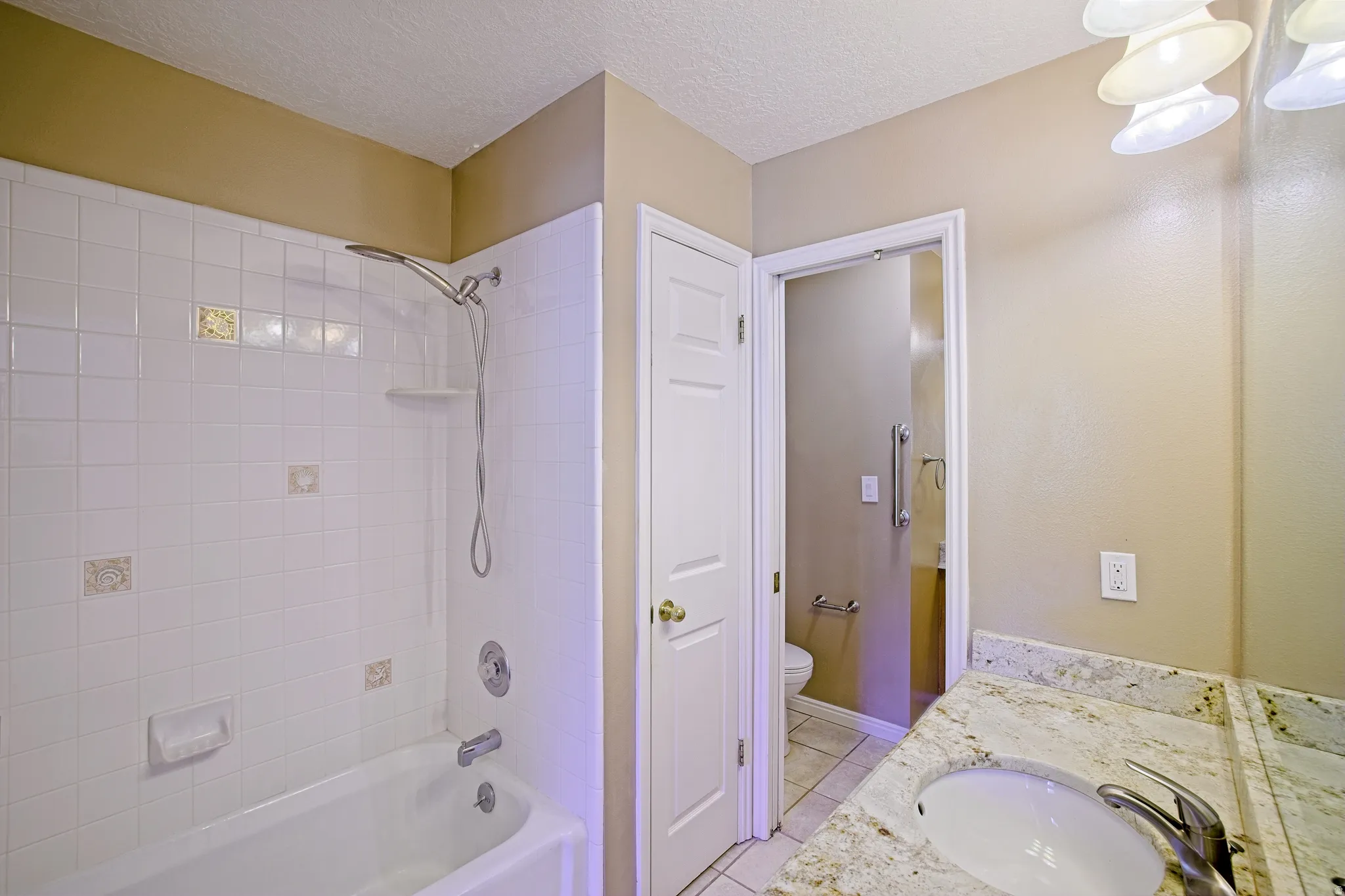 Bathroom featuring a shower-over-tub combination with white subway tile, a vanity with a stone-finish countertop, an undermount sink, and a chrome faucet