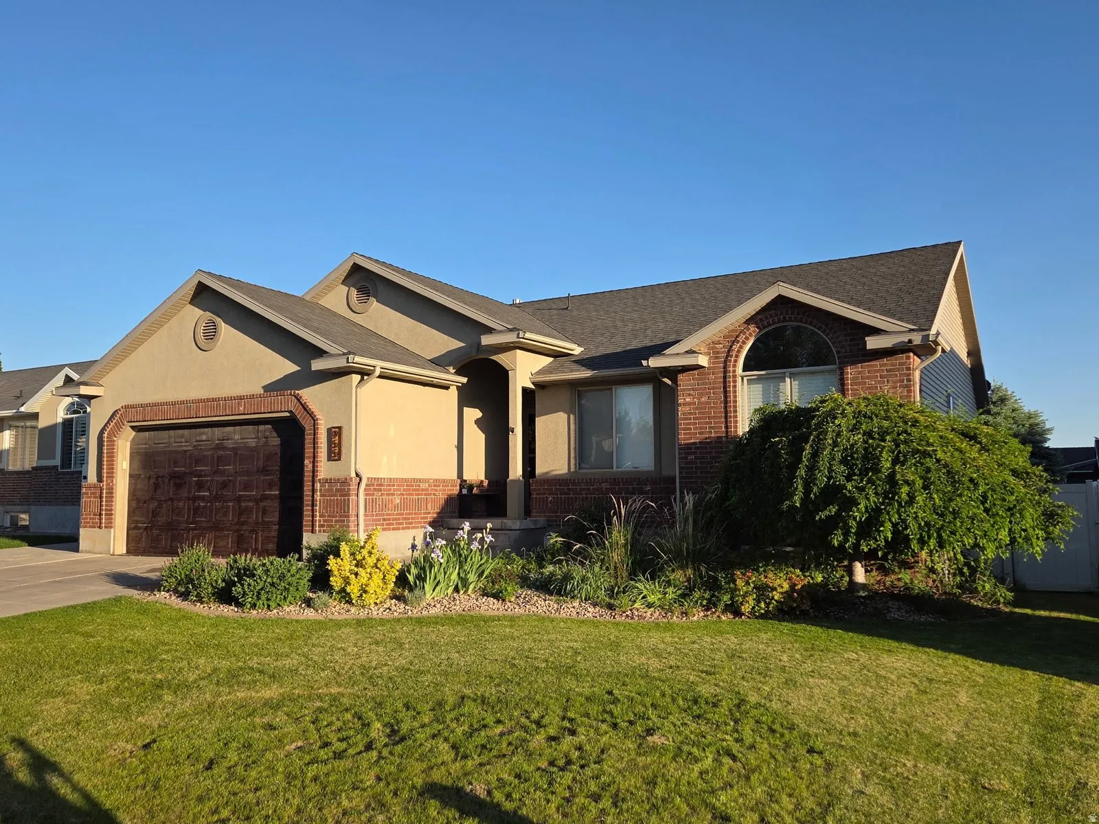 Exterior featuring brick and stucco accents, an attached garage, landscaped front yard, arched window, and prominent front entry
