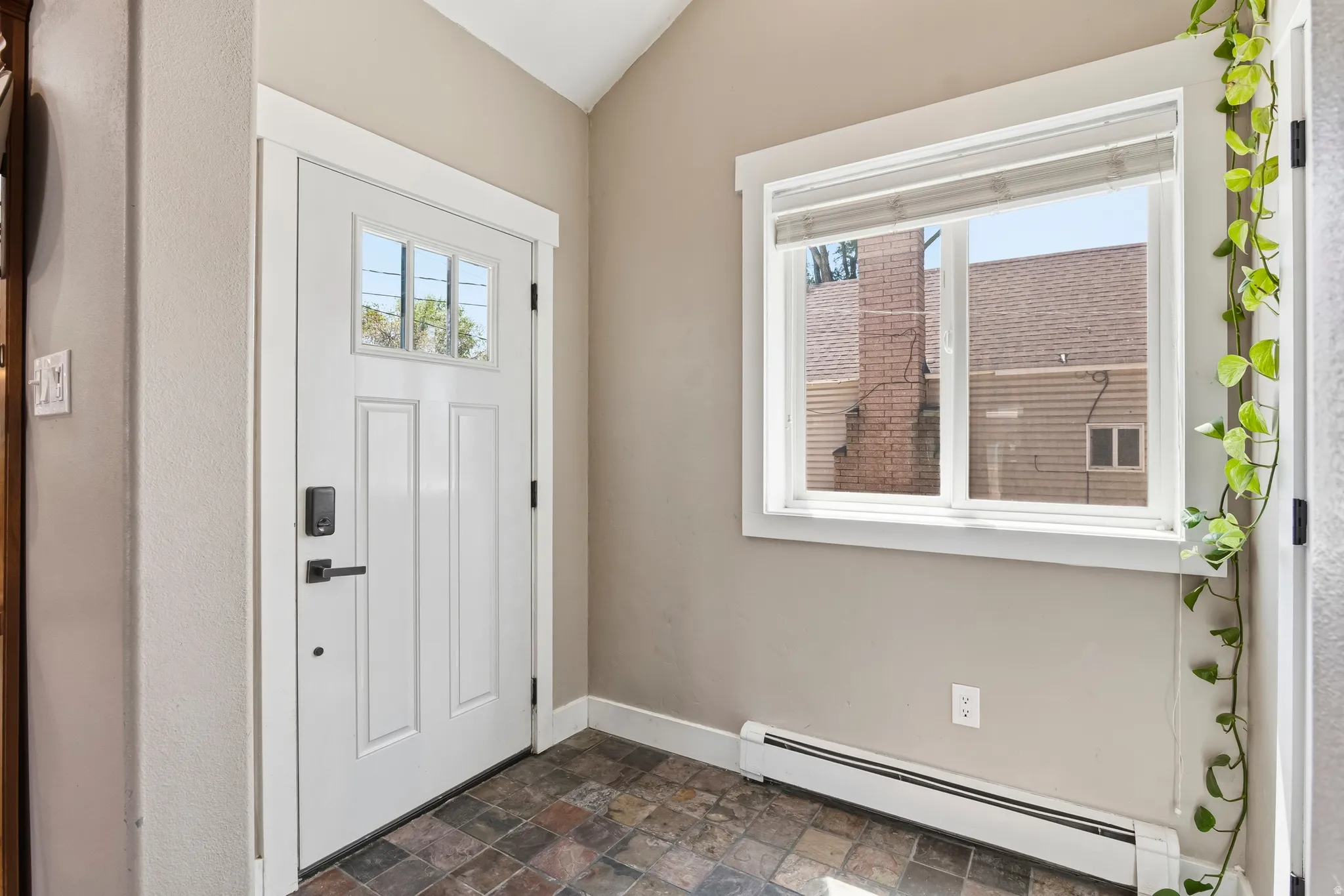 Entryway featuring a white paneled door with glass inserts and dark hardware, stone-finish tile flooring, a horizontal window with blinds, and painted walls
