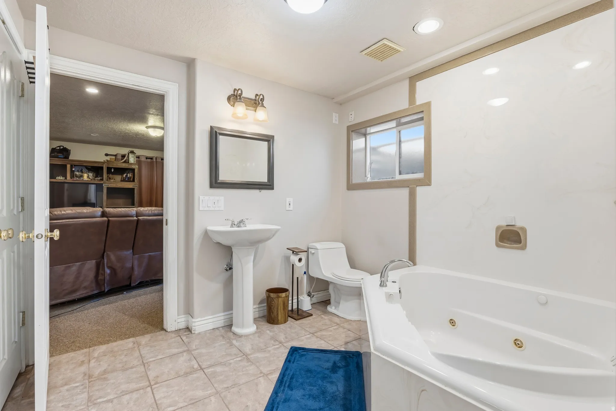 Bathroom featuring a white pedestal sink, a jetted corner bathtub, and a window with frosted glass