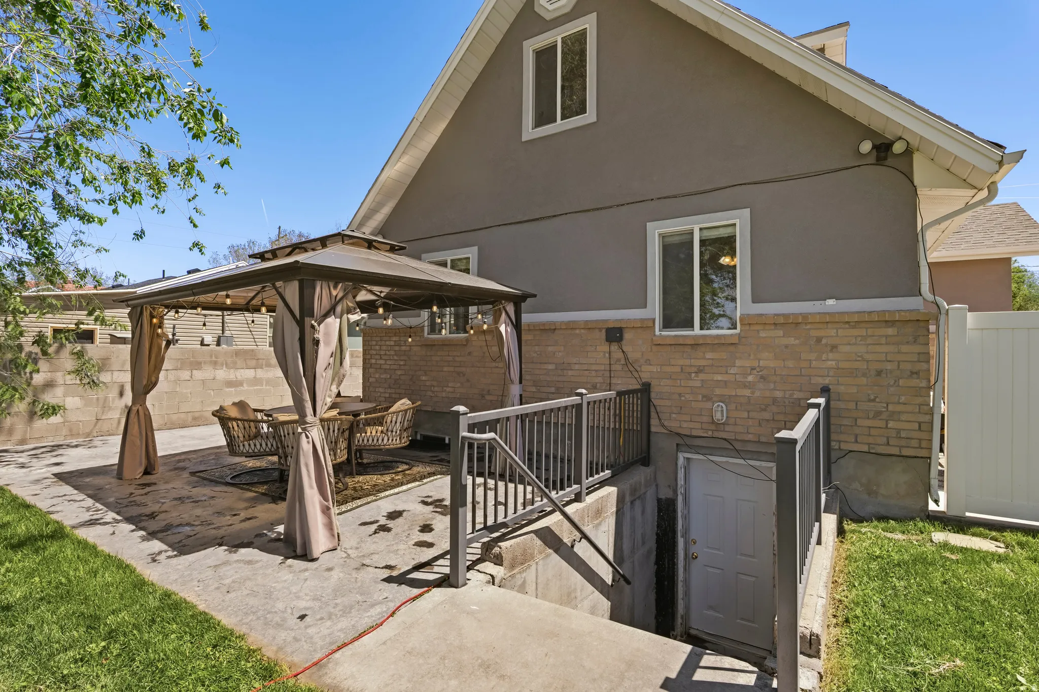 Rear exterior featuring a concrete patio, a gazebo structure, and a basement access point with railings