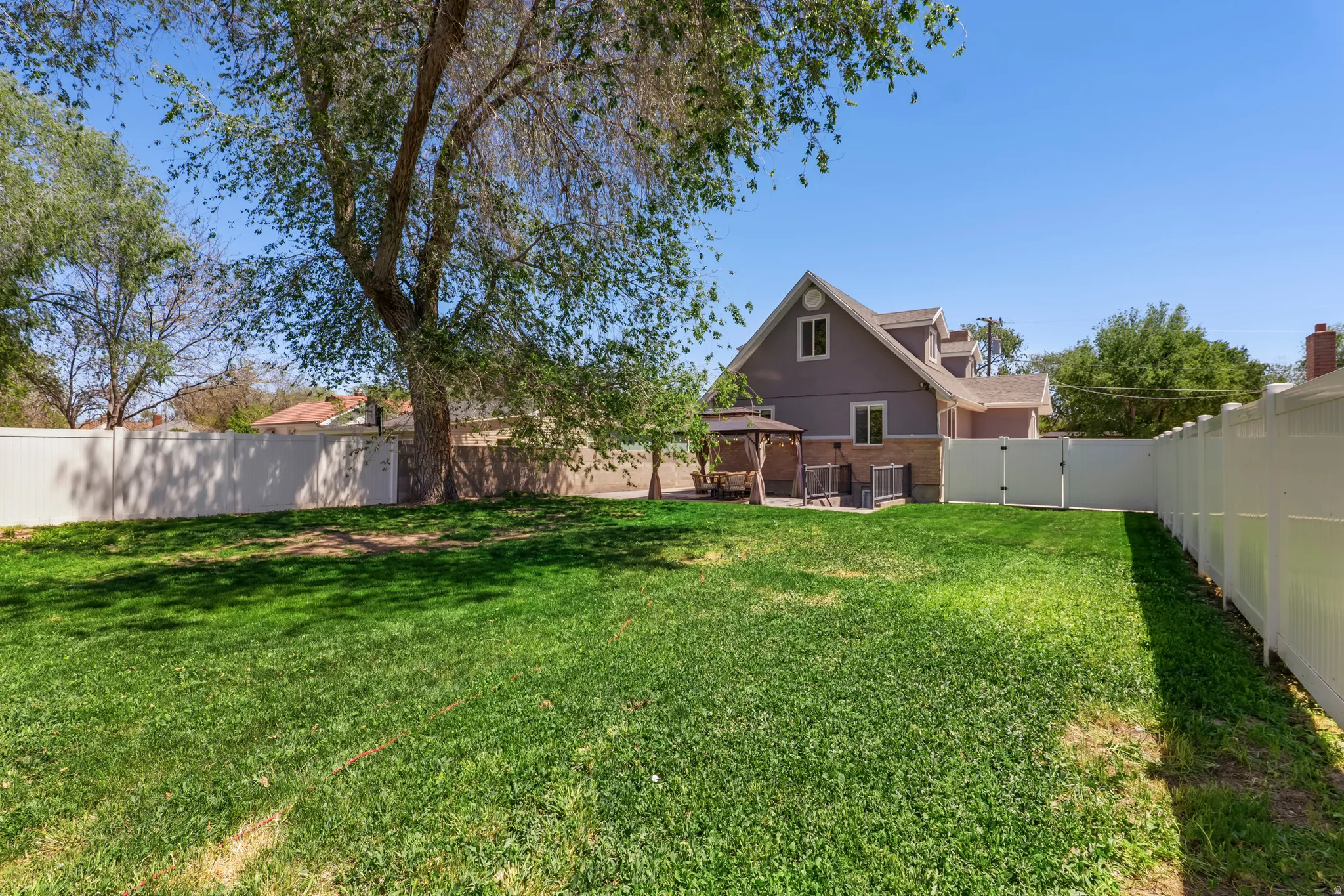 Expansive backyard featuring a lush lawn, mature trees providing natural shade, and complete privacy fencing