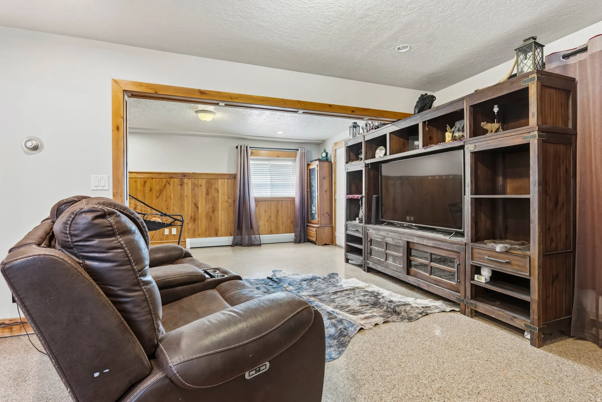 Spacious interior featuring wood-finish flooring, a wood-paneled accent wall, and a large built-in media console with shelving