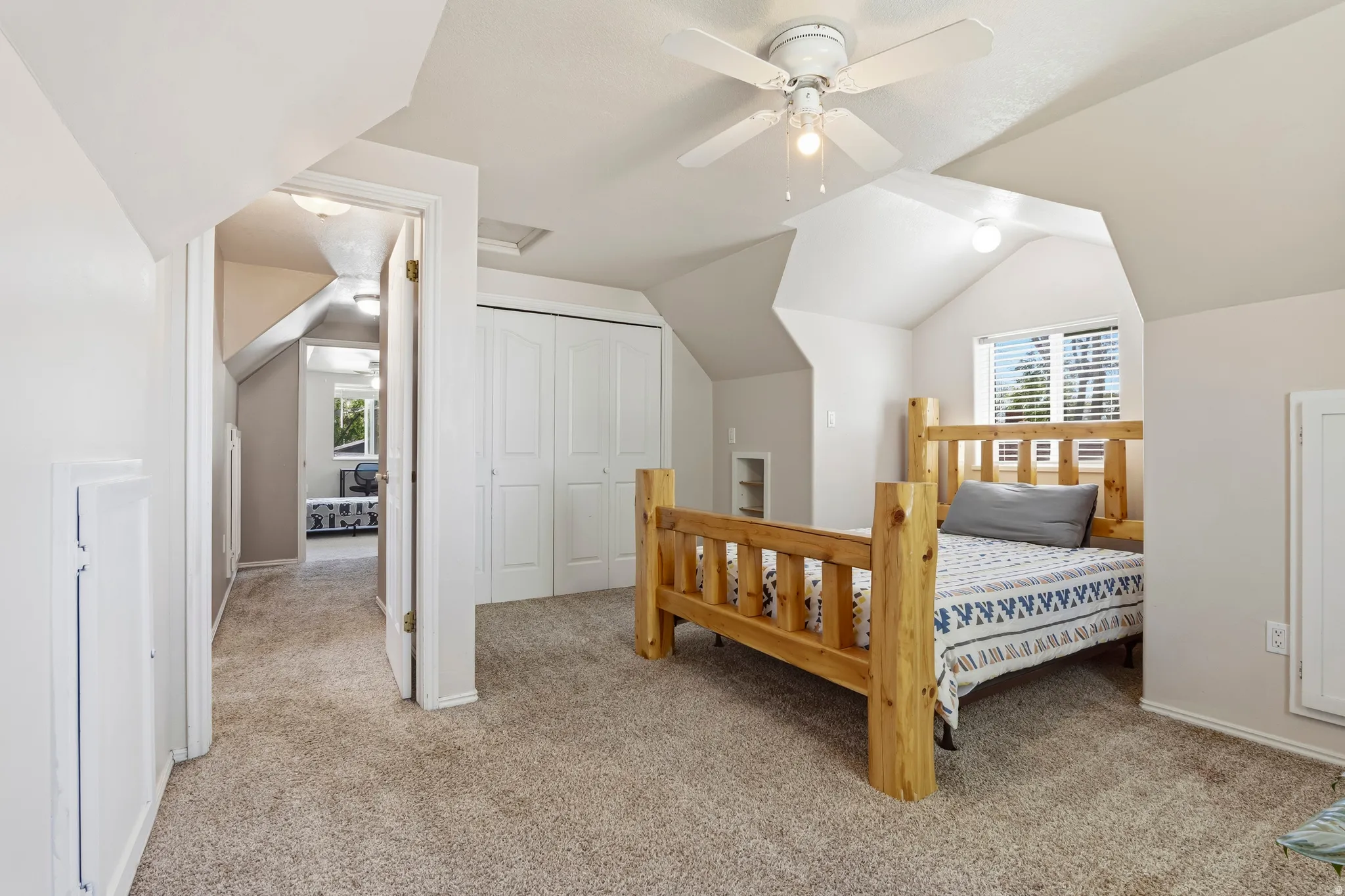 Carpeted room with a vaulted ceiling, a window featuring blinds, a ceiling fan with integrated lighting, and white bi-fold closet doors