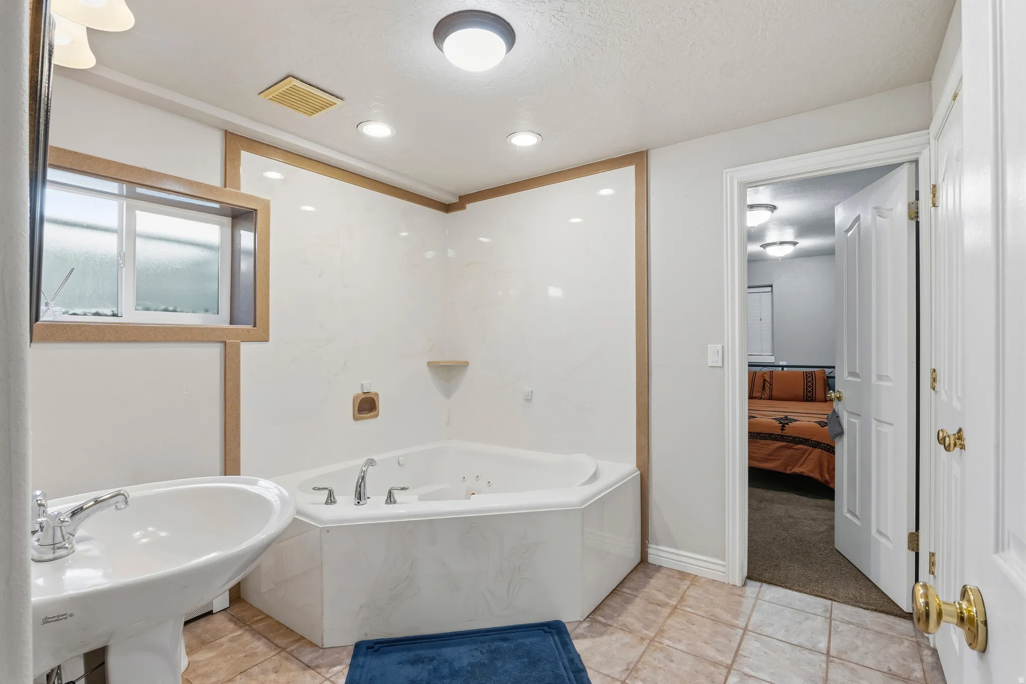 Bathroom featuring a corner jetted tub with wall-mounted fixtures, pedestal sink with chrome faucet, tiled flooring, and recessed lighting