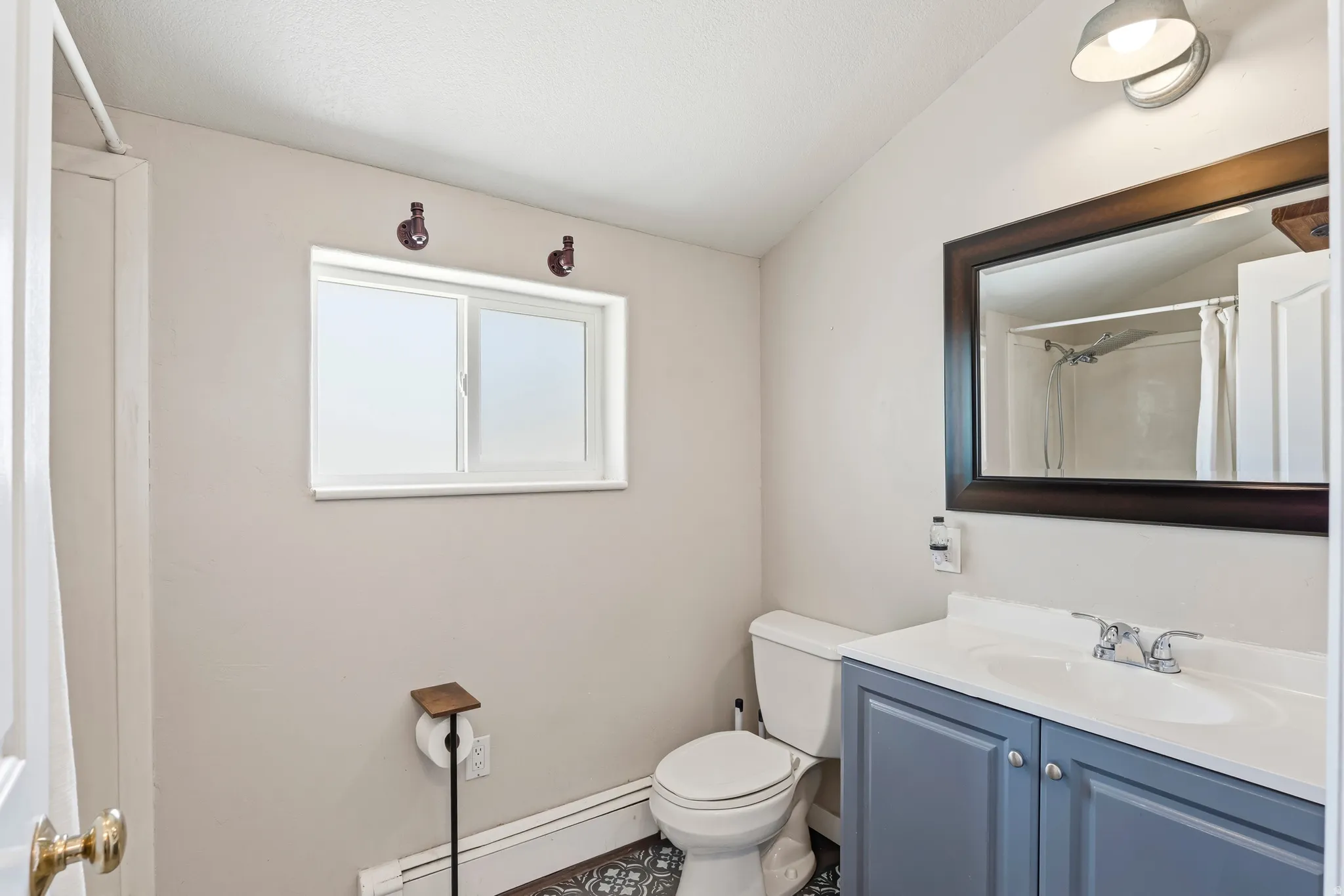 Bathroom featuring a single window, a light blue vanity with integrated sink, a dark framed mirror, and patterned floor tiles