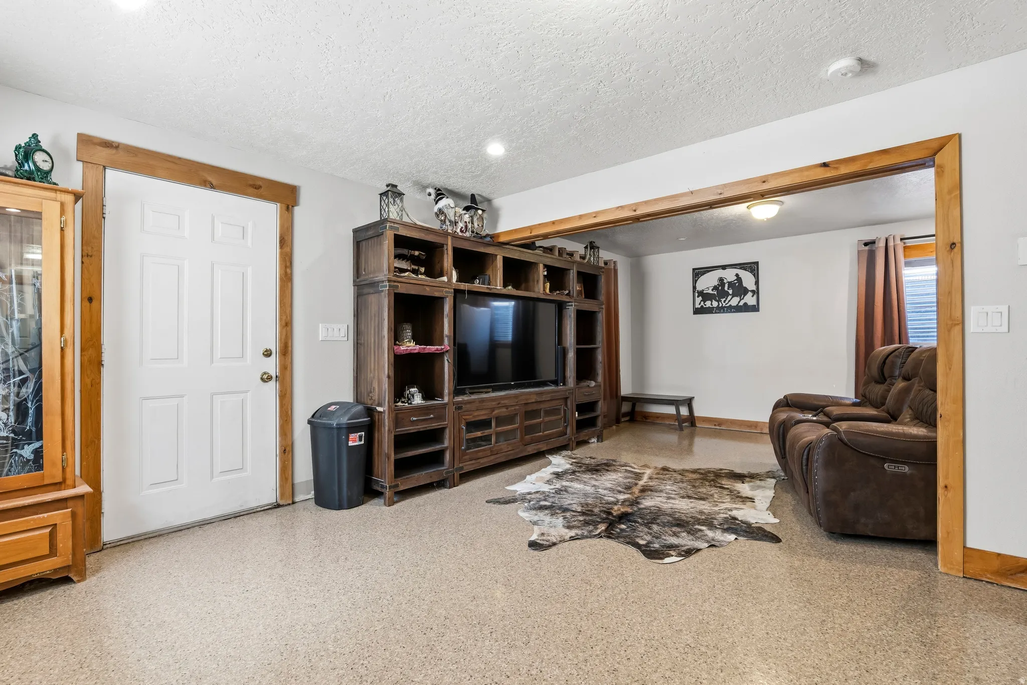 Spacious room featuring light-colored flooring, a white paneled door with wood trim, and a built-in wood entertainment center