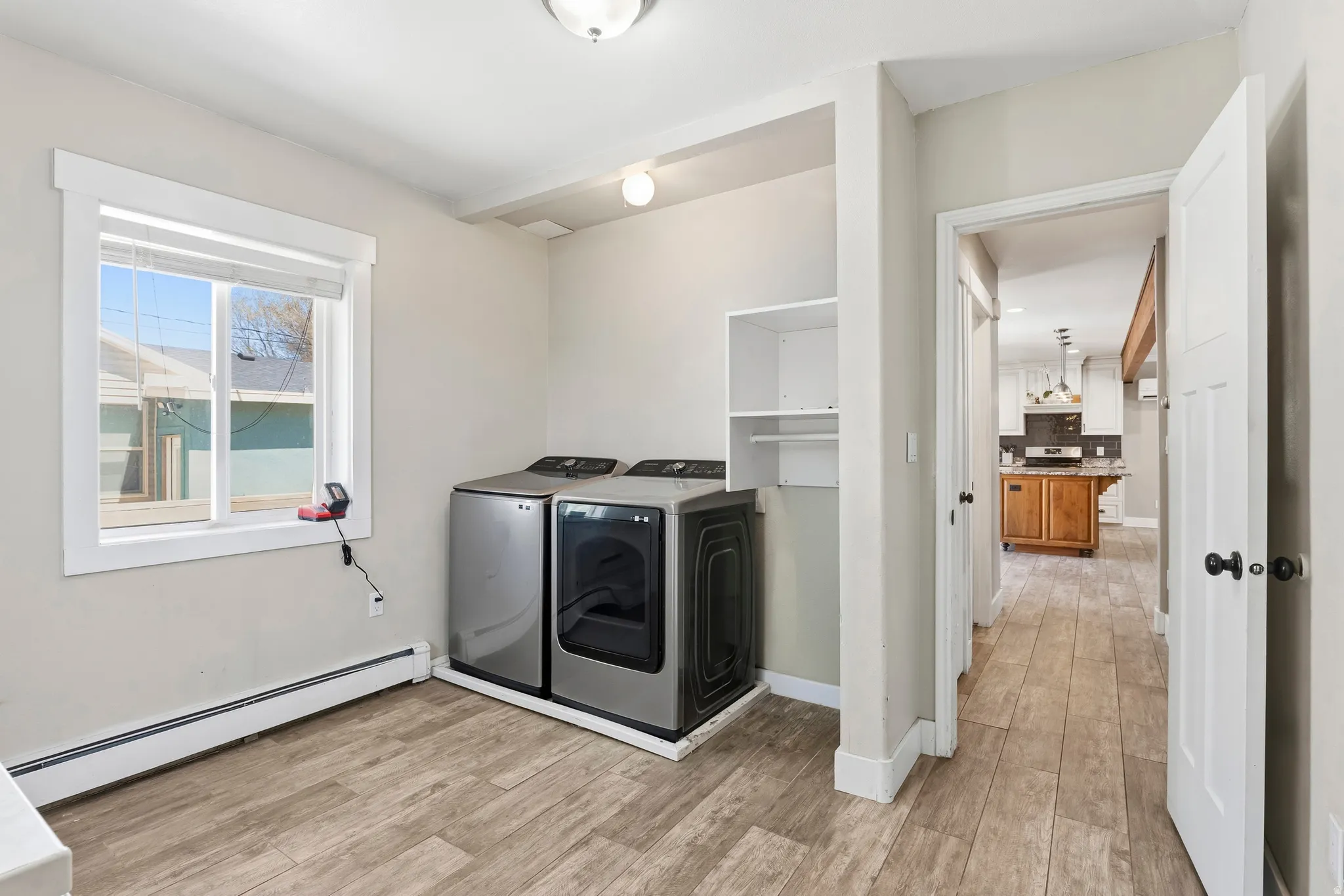 Utility room featuring wood-finish flooring, a window with white trim, built-in shelving, and a baseboard radiator