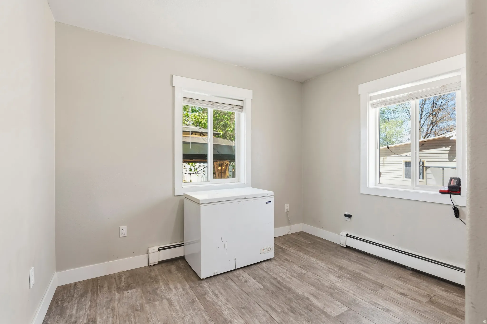 Room featuring two windows with white trim, light gray walls, white baseboards, and wood-finish flooring