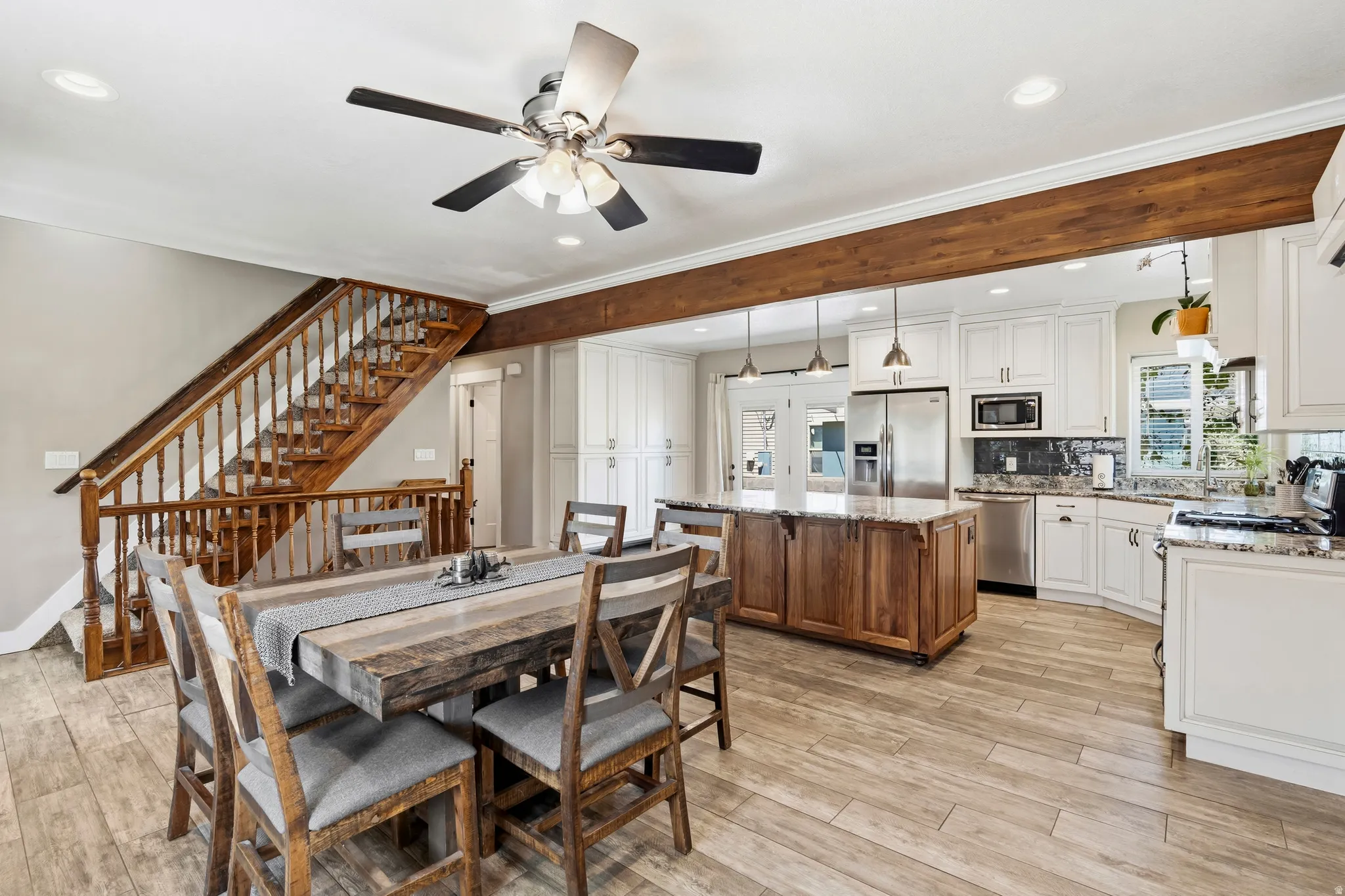 Open-concept living space featuring wood-finish flooring, a substantial wood staircase with banister, and a kitchen with white cabinetry and stainless steel appliances