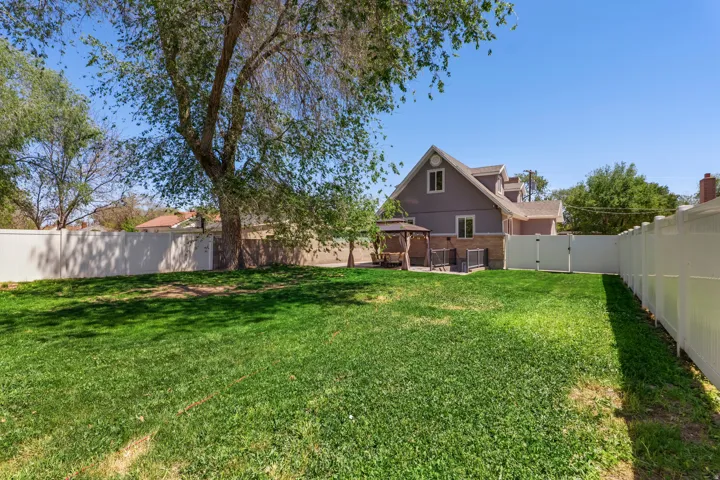 Expansive backyard featuring a lush lawn, mature trees providing natural shade, and complete privacy fencing