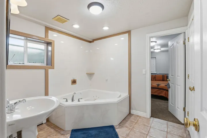 Bathroom featuring a corner jetted tub with wall-mounted fixtures, pedestal sink with chrome faucet, tiled flooring, and recessed lighting