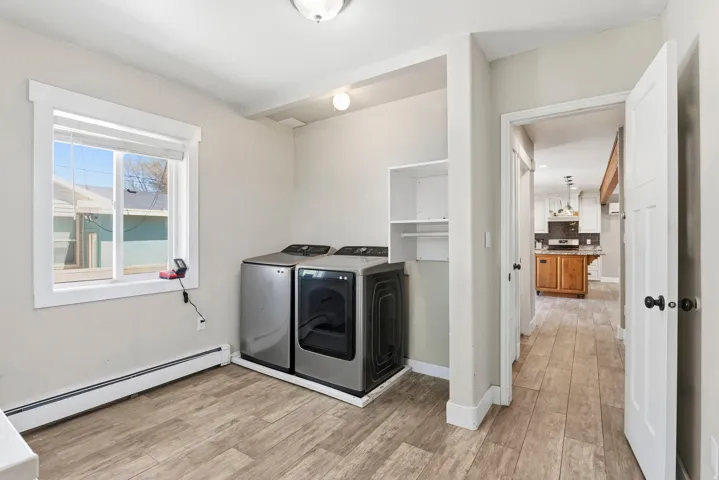 Utility room featuring wood-finish flooring, a window with white trim, built-in shelving, and a baseboard radiator