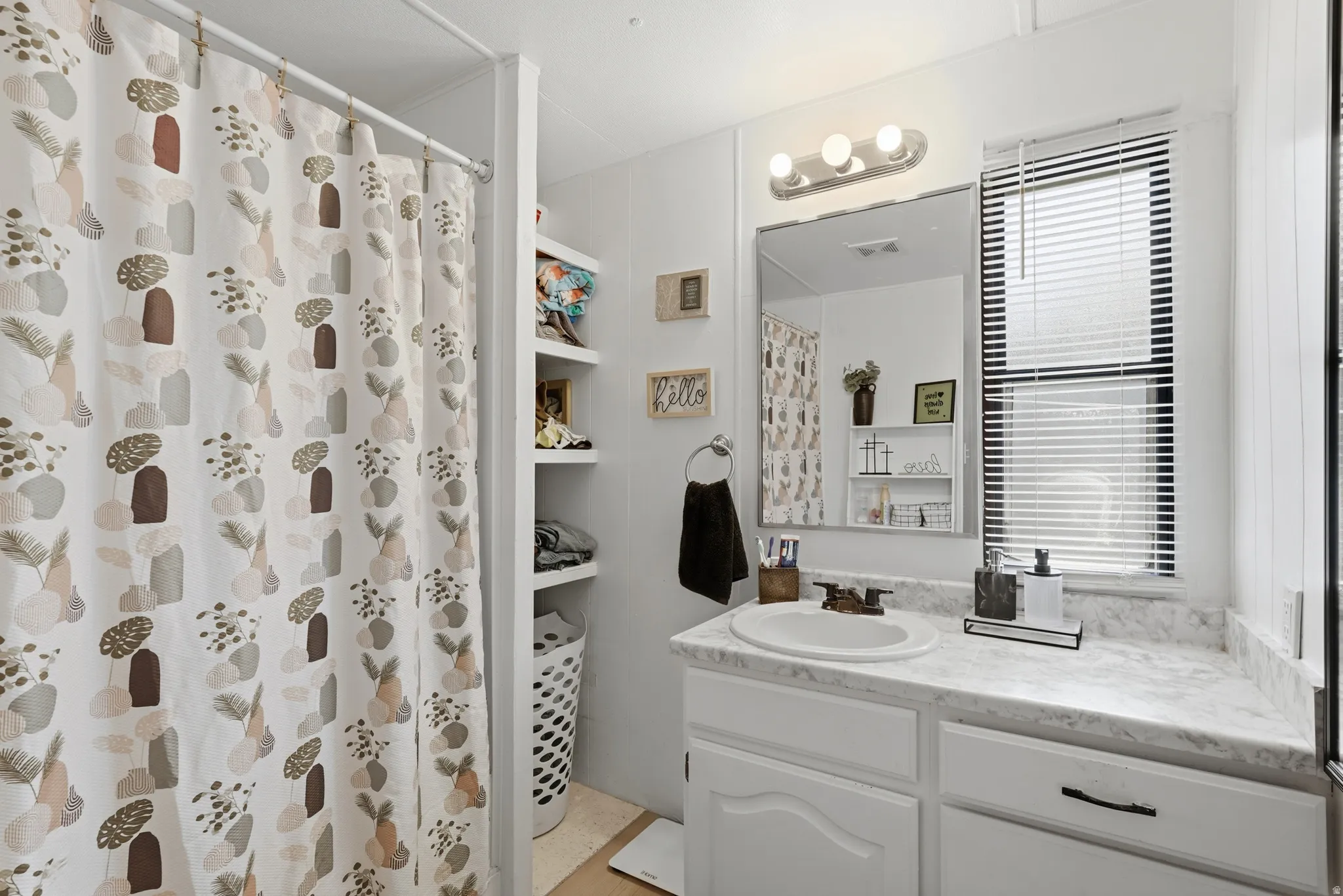 Bathroom featuring a white vanity with an integrated sink, a light-toned countertop, and white cabinetry with dark hardware
